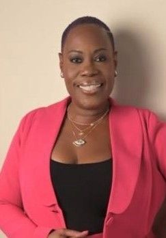 Woman in pink blazer and black top smiles, standing against a neutral background.