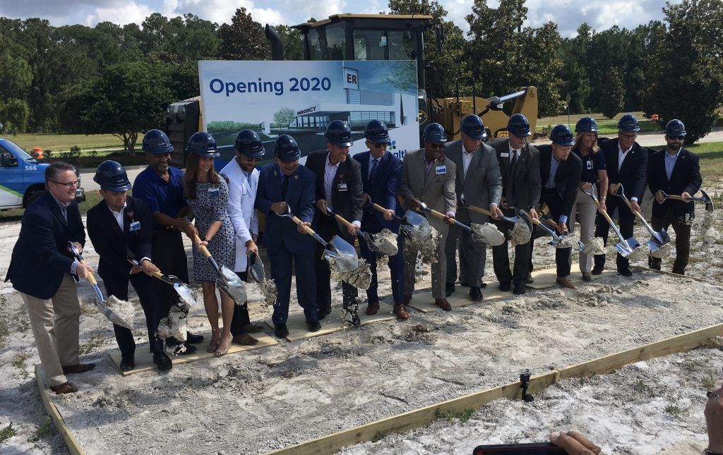 People with shovels at a groundbreaking ceremony, digging into dirt, with a sign that says 