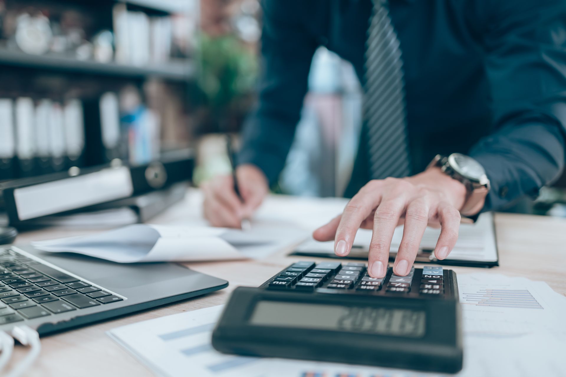 Un uomo usa una calcolatrice mentre scrive su un pezzo di carta.