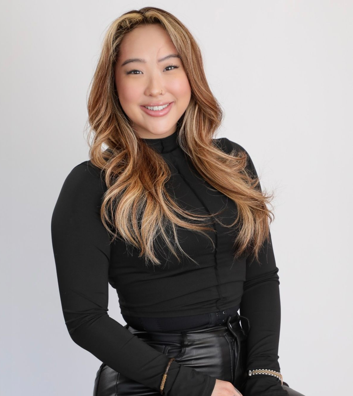 Woman smiling, holding a phone, wearing a black blazer with feather detail, in a building with a wooden staircase, framed.