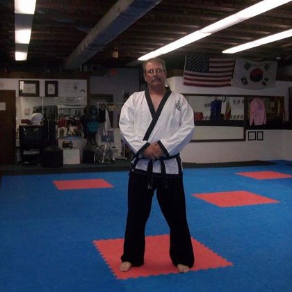 A man in a karate uniform is standing on a mat in a gym