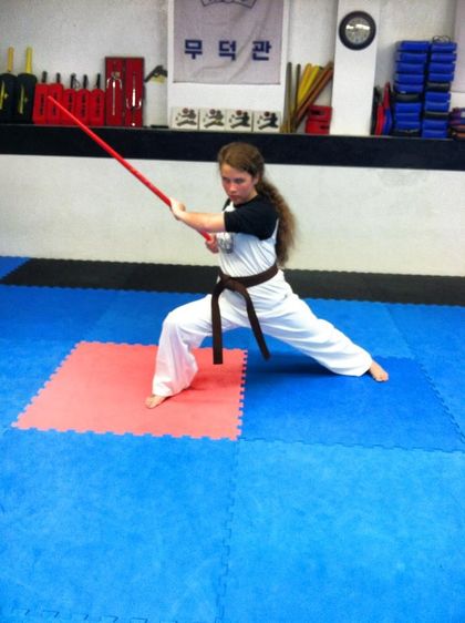 A young girl is practicing martial arts with a red stick
