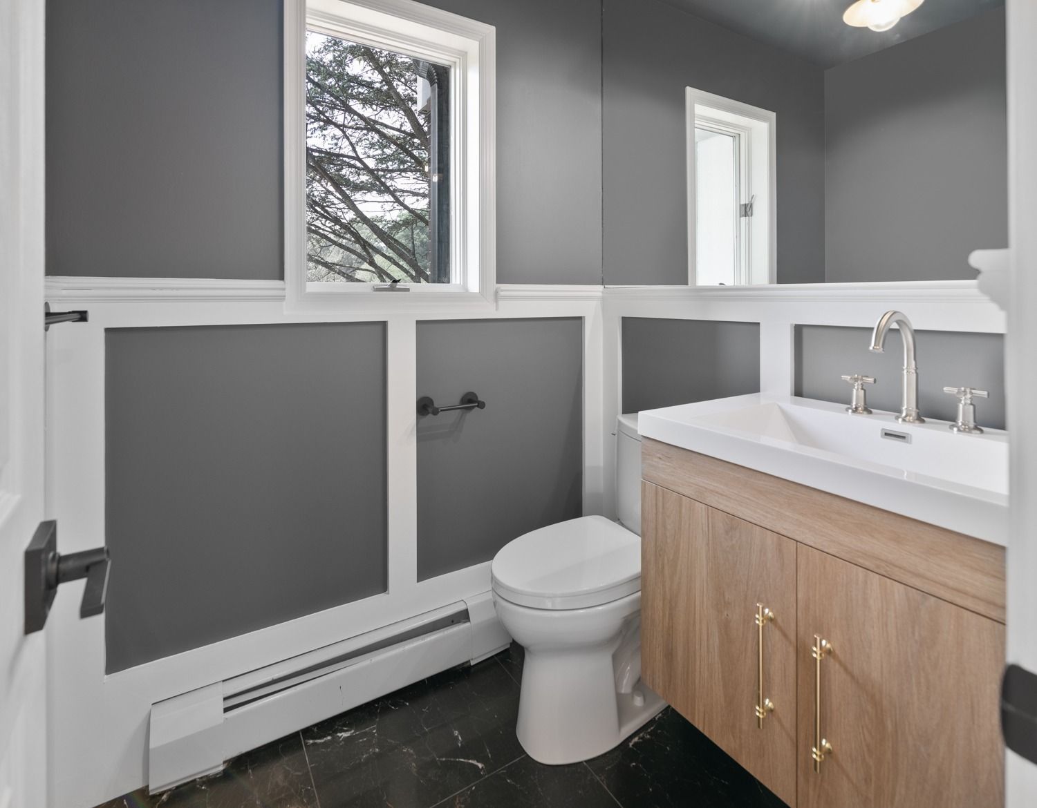 Bathroom with gray walls, white trim, wood vanity, toilet, and window.