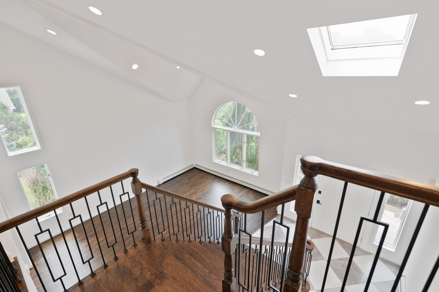 High-angle view of a stairway with dark wood railing and floor, leading to a bright, arched window and skylight.