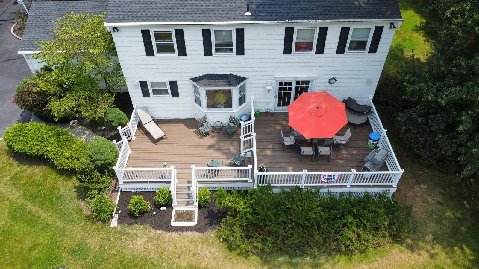 Two-story white house with a deck, red umbrella, and outdoor seating in the backyard.