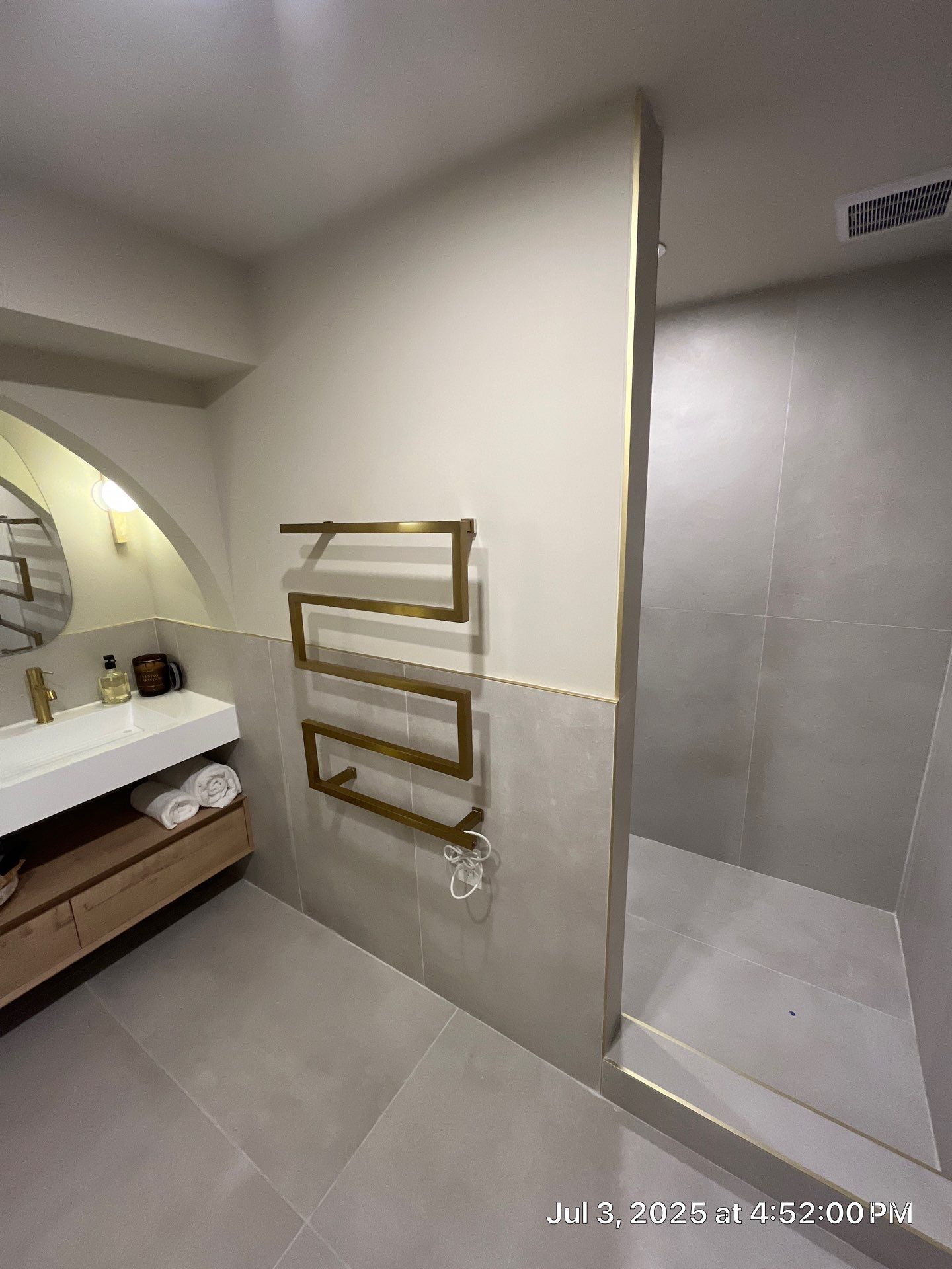 Modern bathroom with gold towel warmer, vanity, and shower. Gray and beige tones dominate.