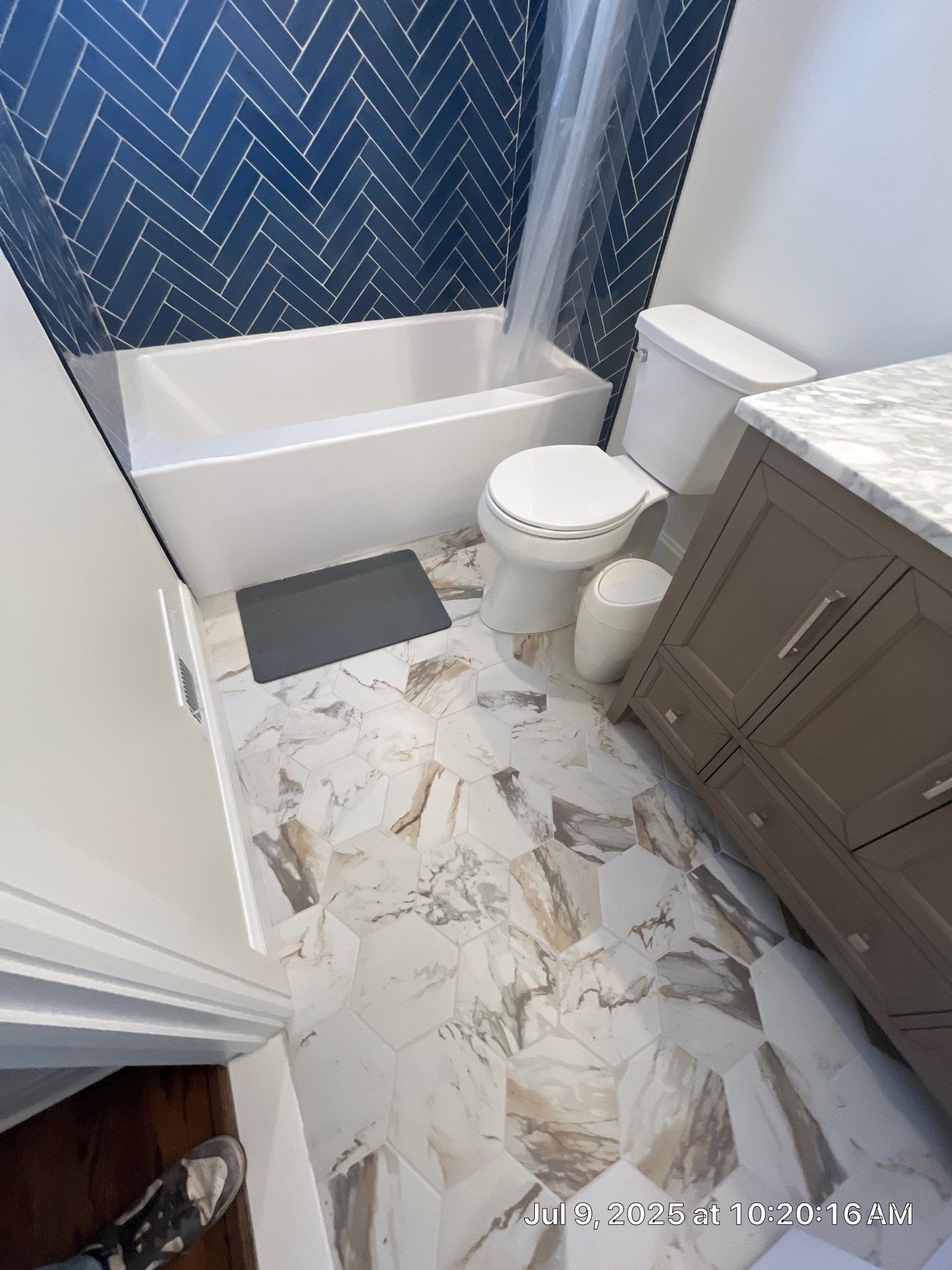 Bathroom with blue herringbone tile, white tub, patterned floor tile, and a gray vanity.