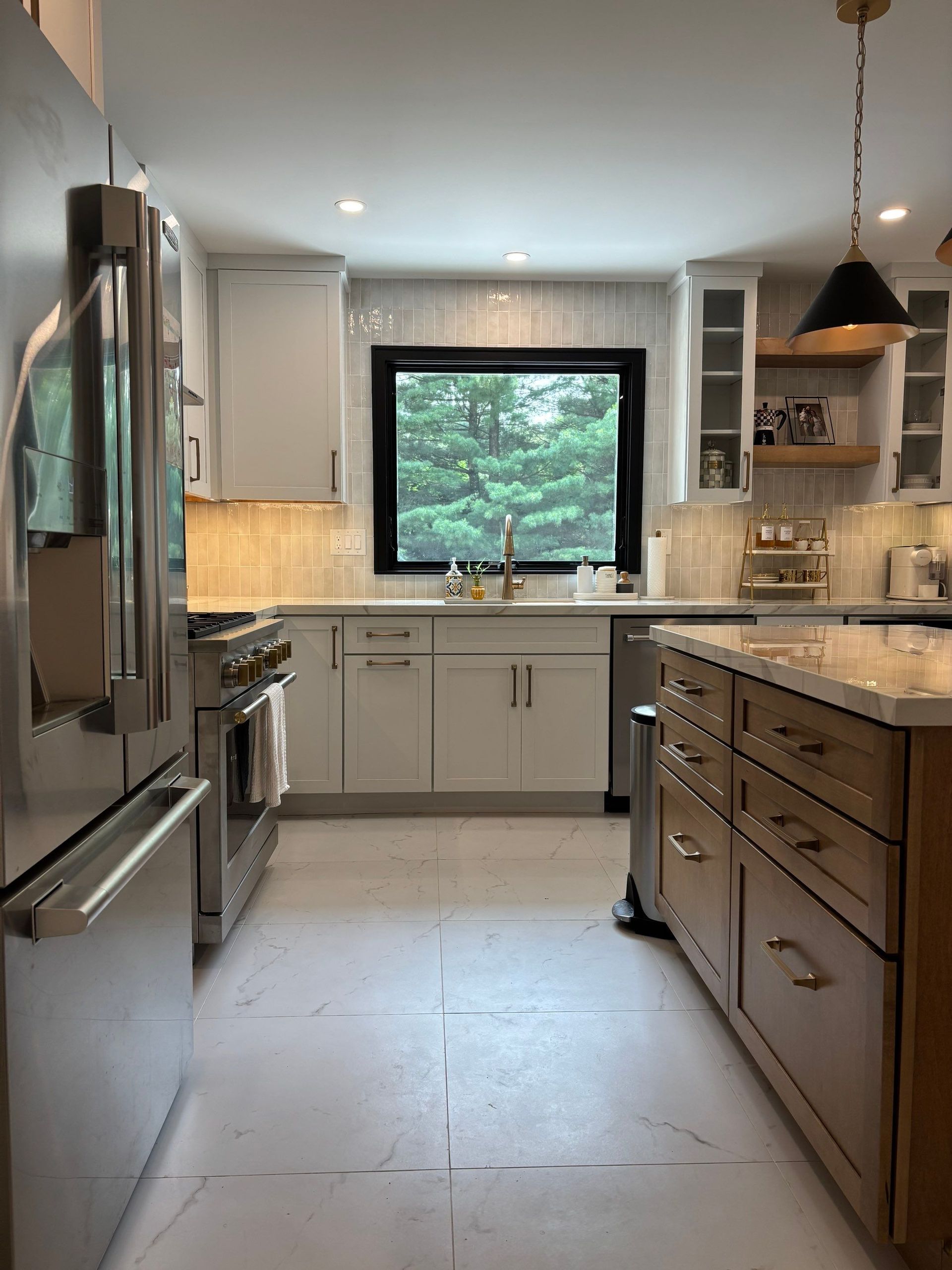 A modern kitchen with stainless steel appliances, white cabinets, and a wooden island. A large window provides natural light.