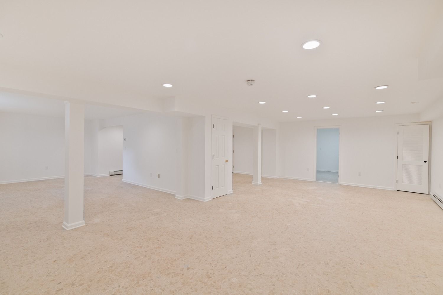 Empty, white-painted basement with carpet flooring and recessed lighting.