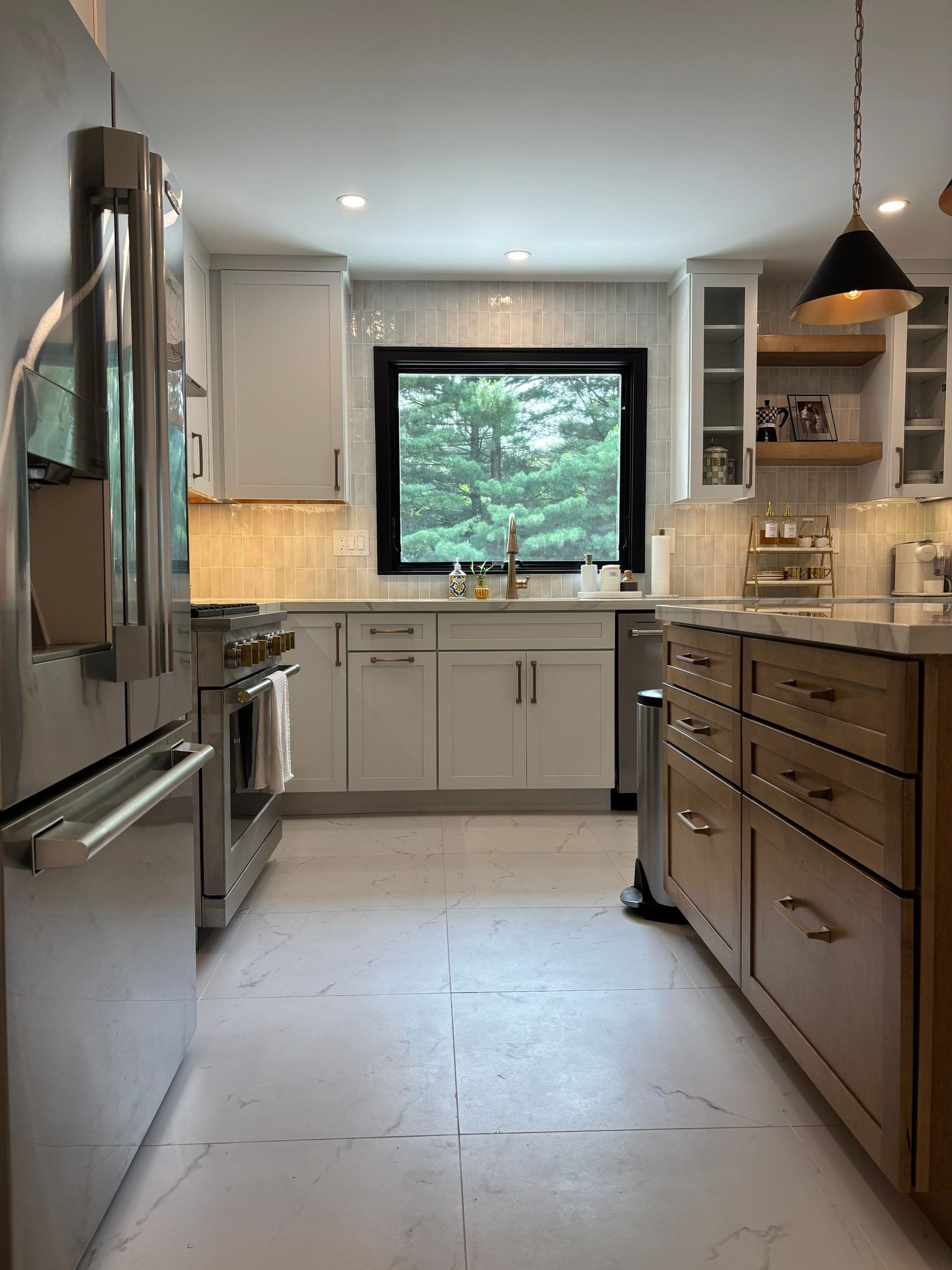 Modern kitchen with stainless steel appliances, white cabinets, and wooden island; a window overlooks greenery.
