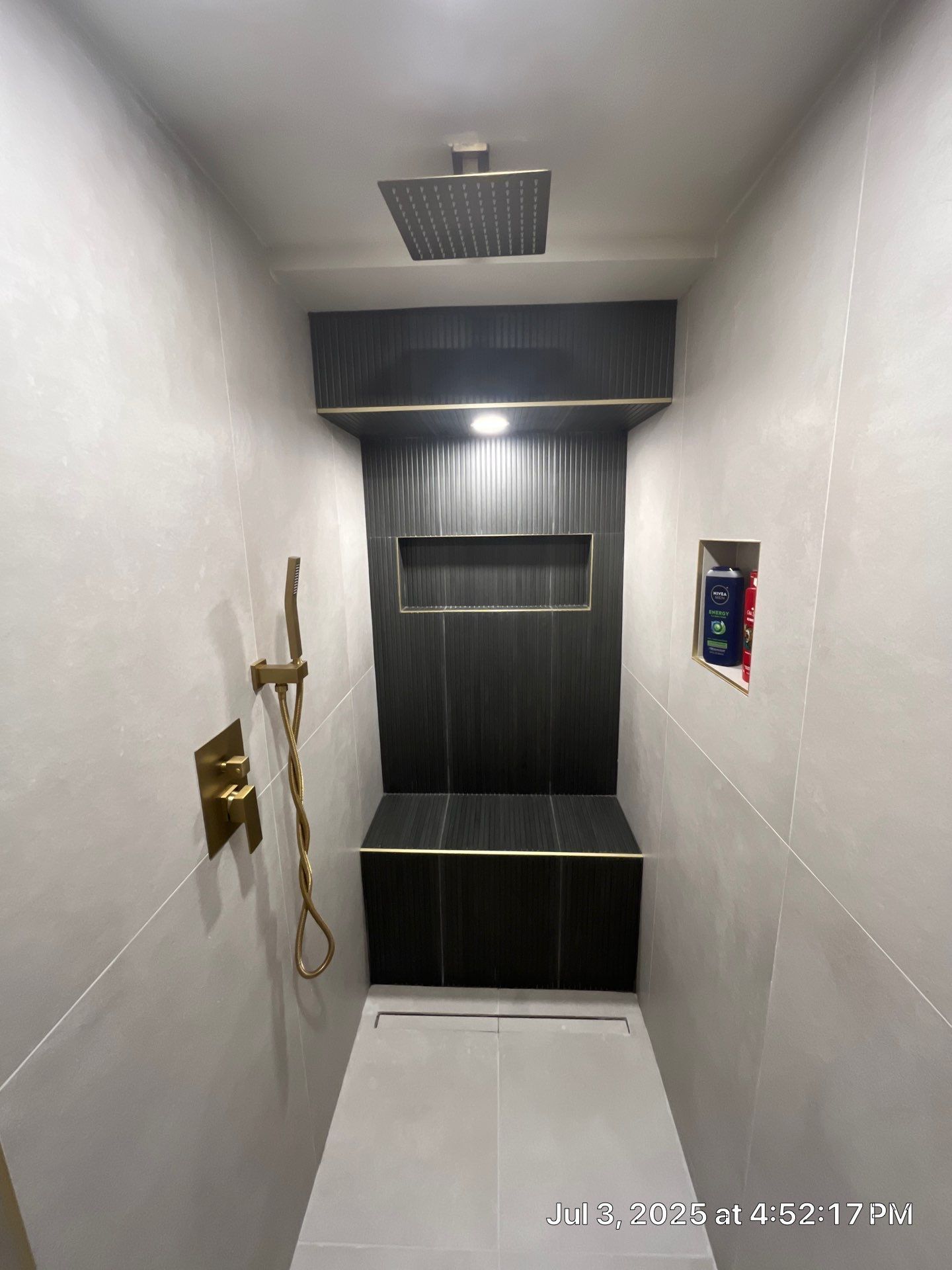Modern shower with gold fixtures, dark tiled niche, and light gray walls.
