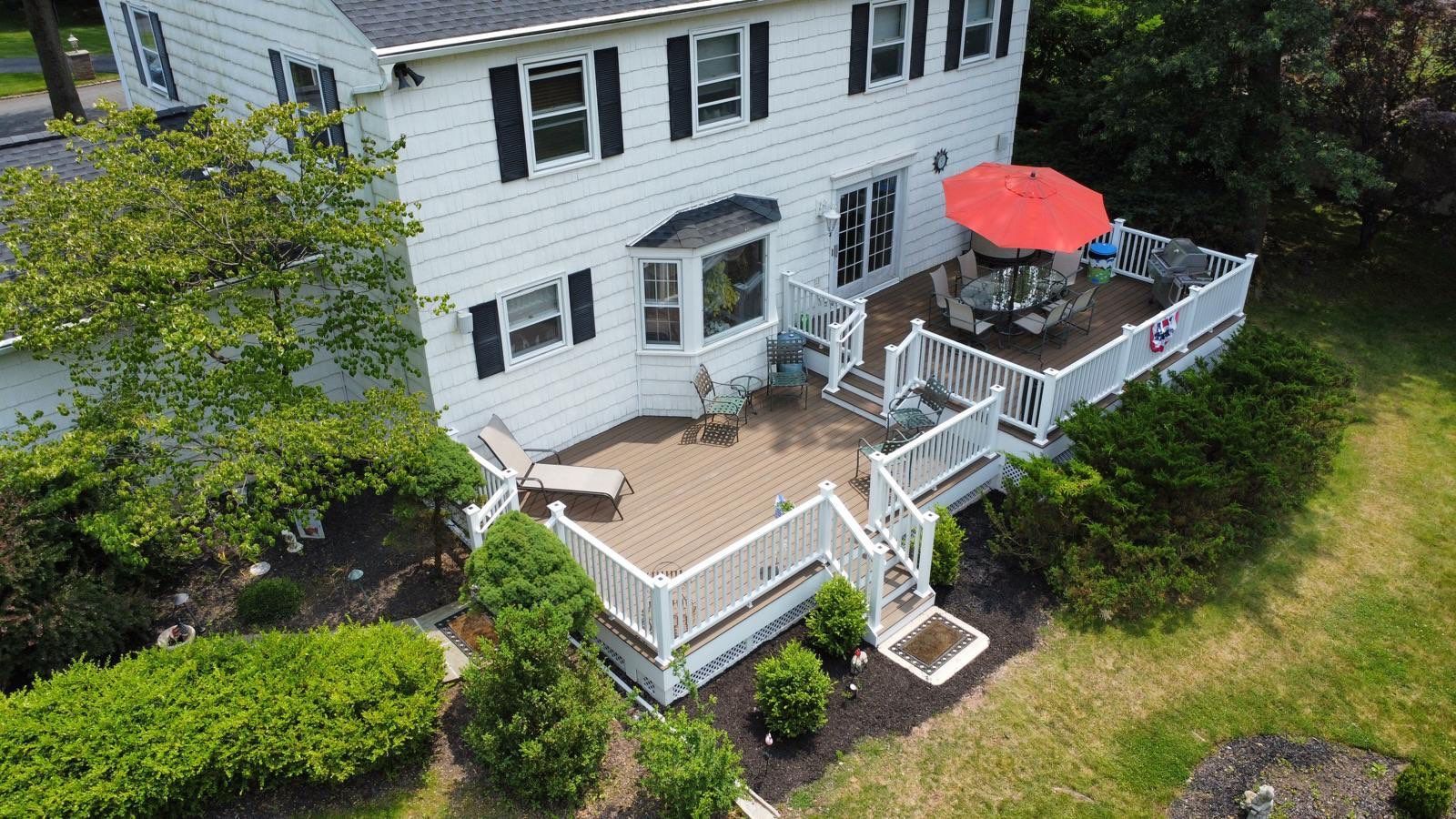 White house with a multi-level deck, brown composite decking, white railings, and red umbrella on a sunny day.