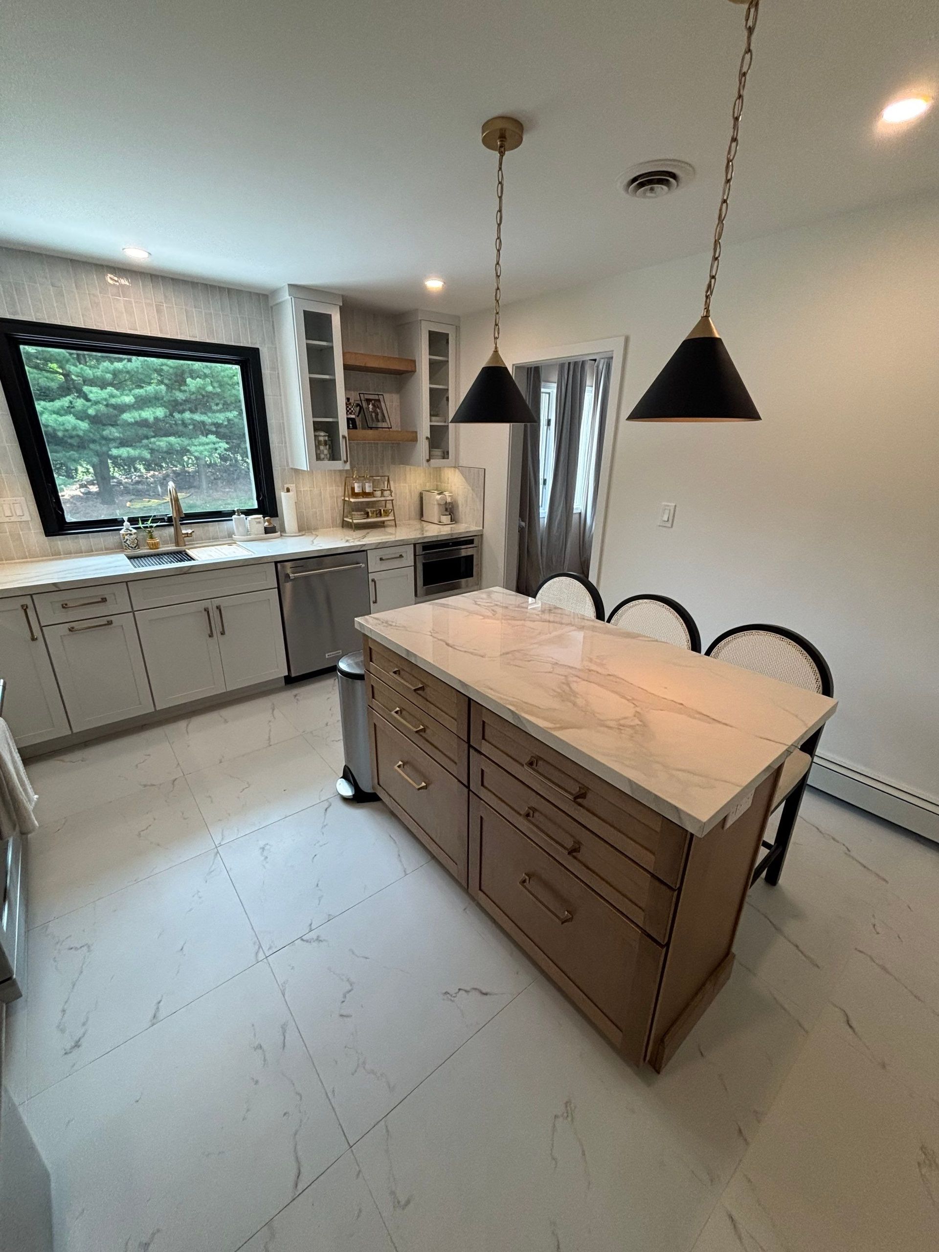 Modern kitchen with island, pendant lights, white cabinets, stainless steel appliances, and a large window.