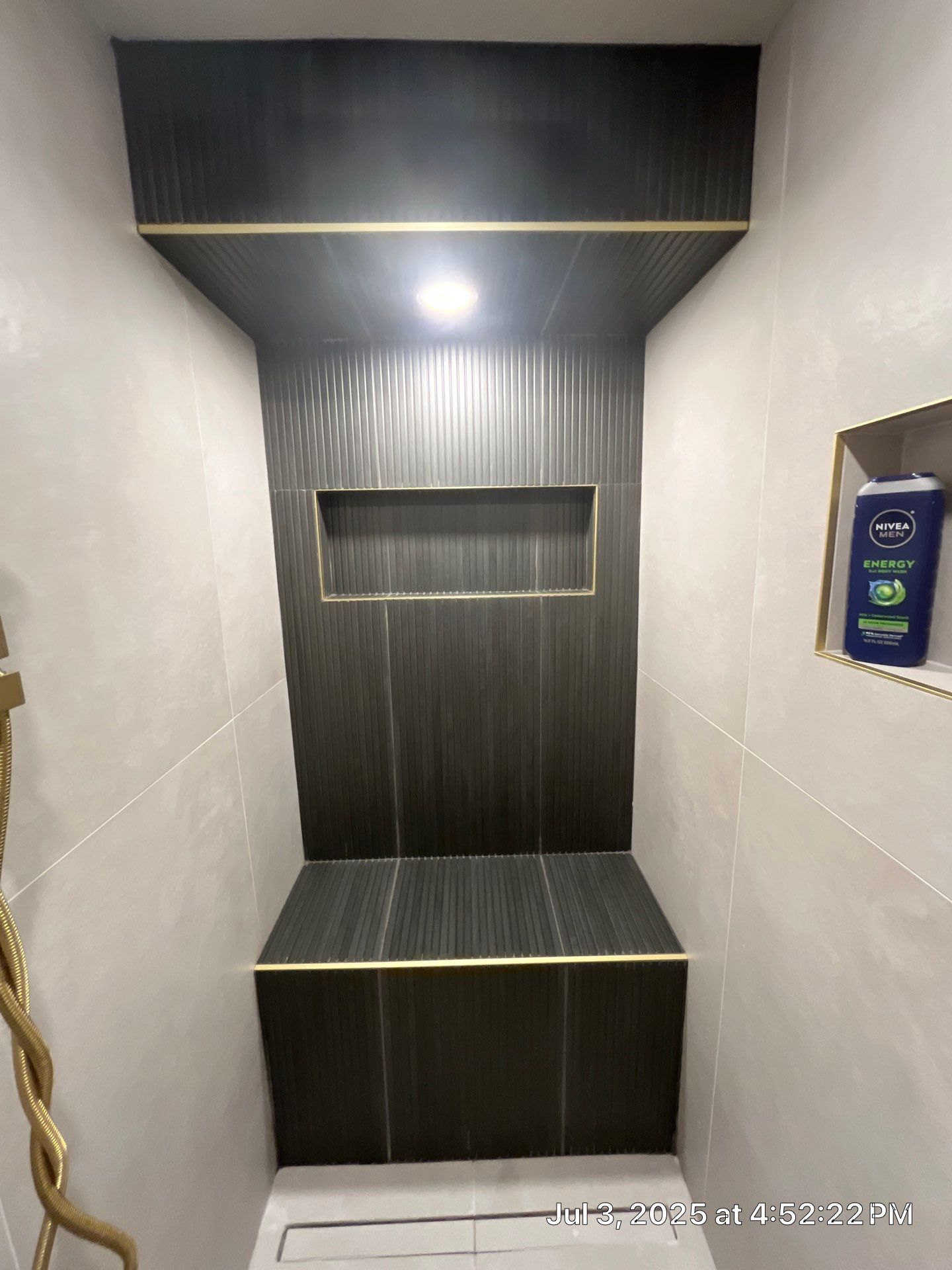 Shower with dark gray accent tiles and brass trim; built-in bench and recessed shelf.