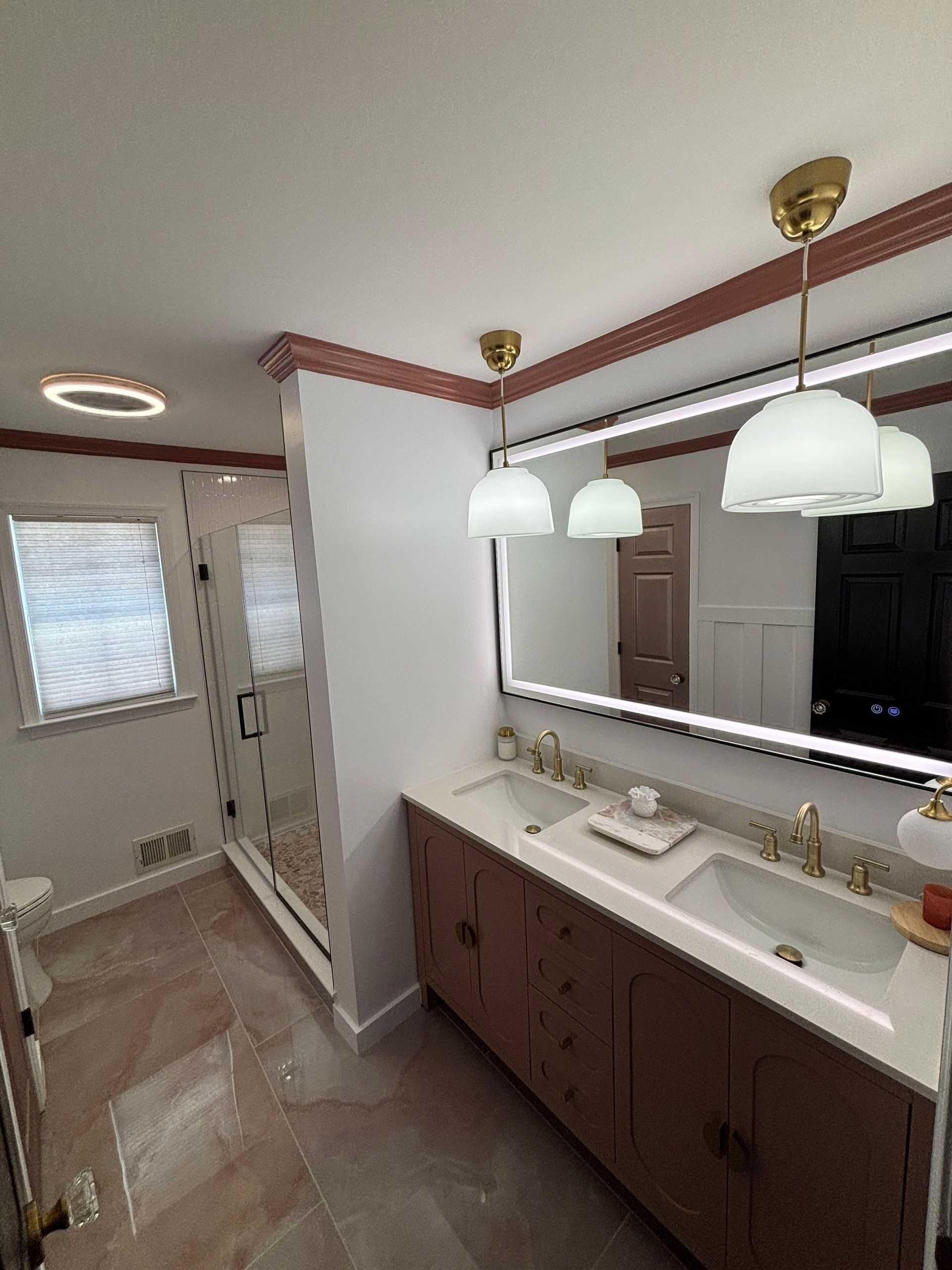 Modern bathroom with double sinks, large mirror, pendant lights, and a shower visible in the background.