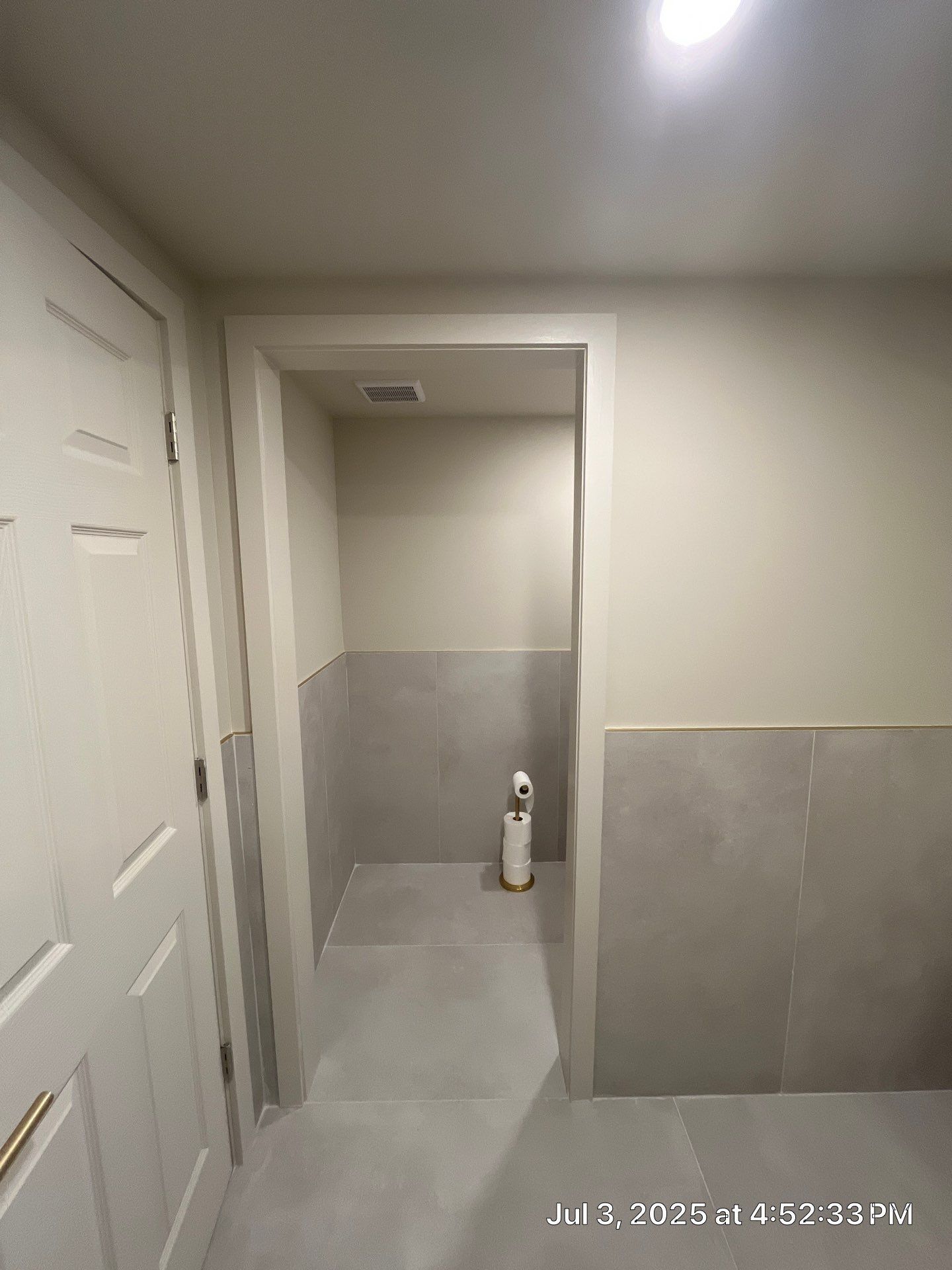Interior of a small bathroom with gray tile wainscotting and a partially open door.