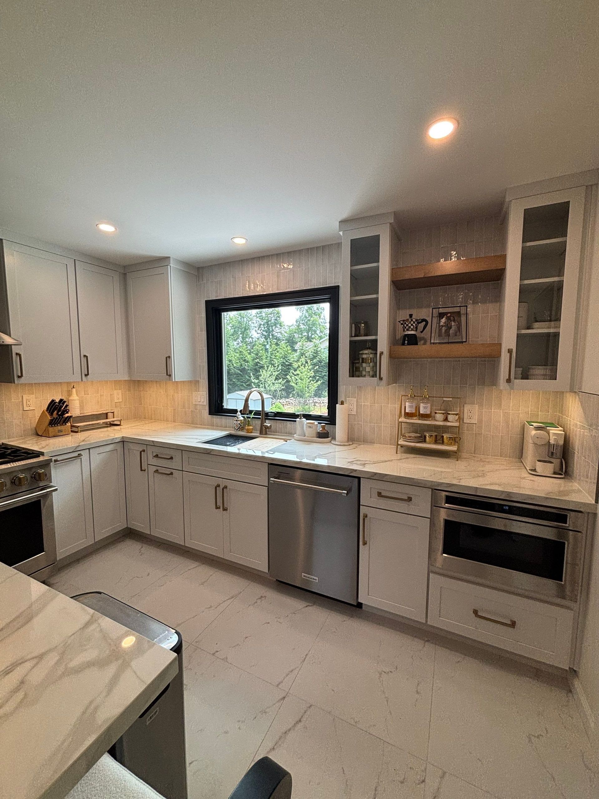 Bright white kitchen with stainless steel appliances, window, and marble countertops.
