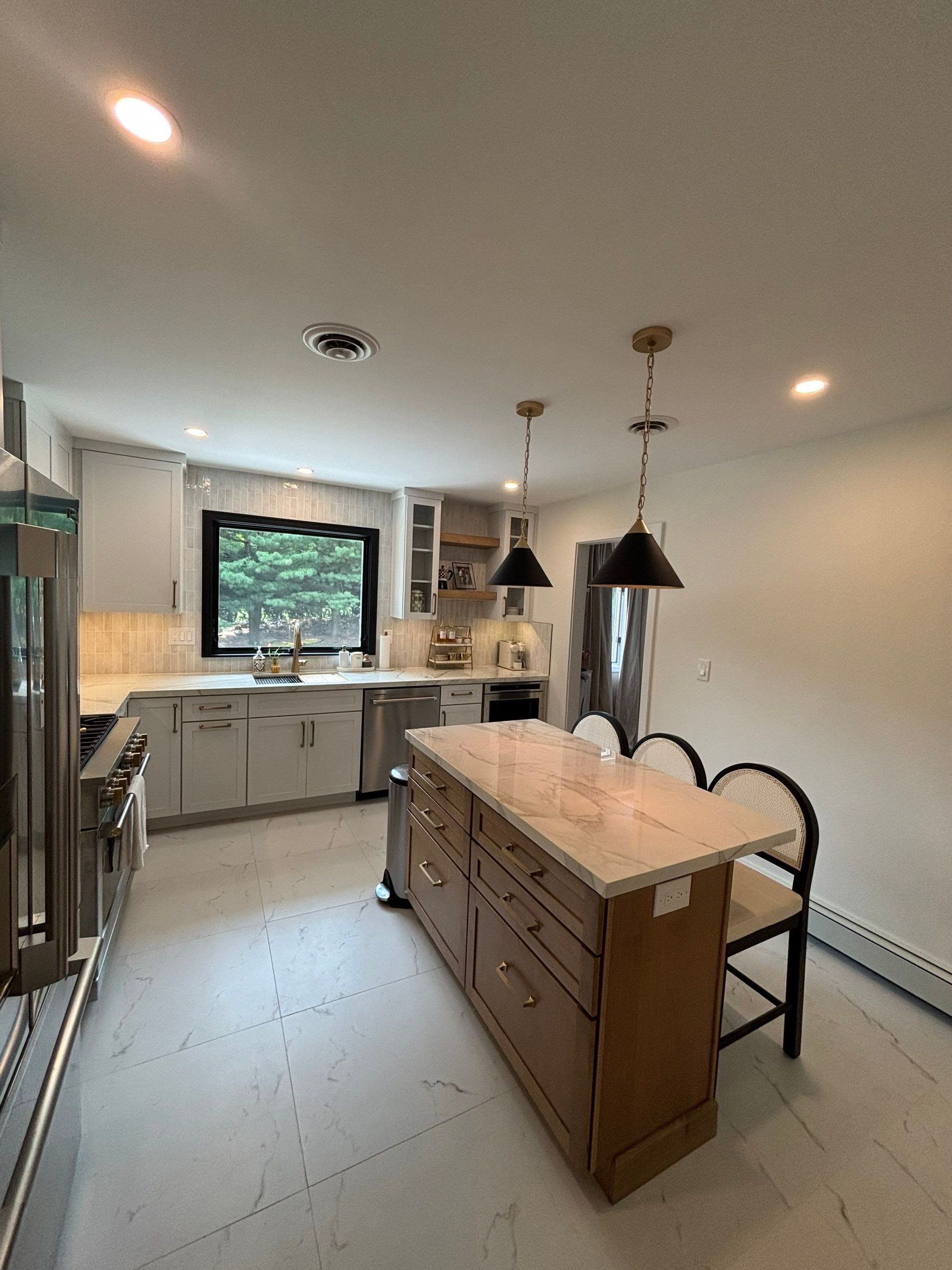 Kitchen with island, light cabinets, and dark pendant lights. White countertops and light-colored floors.