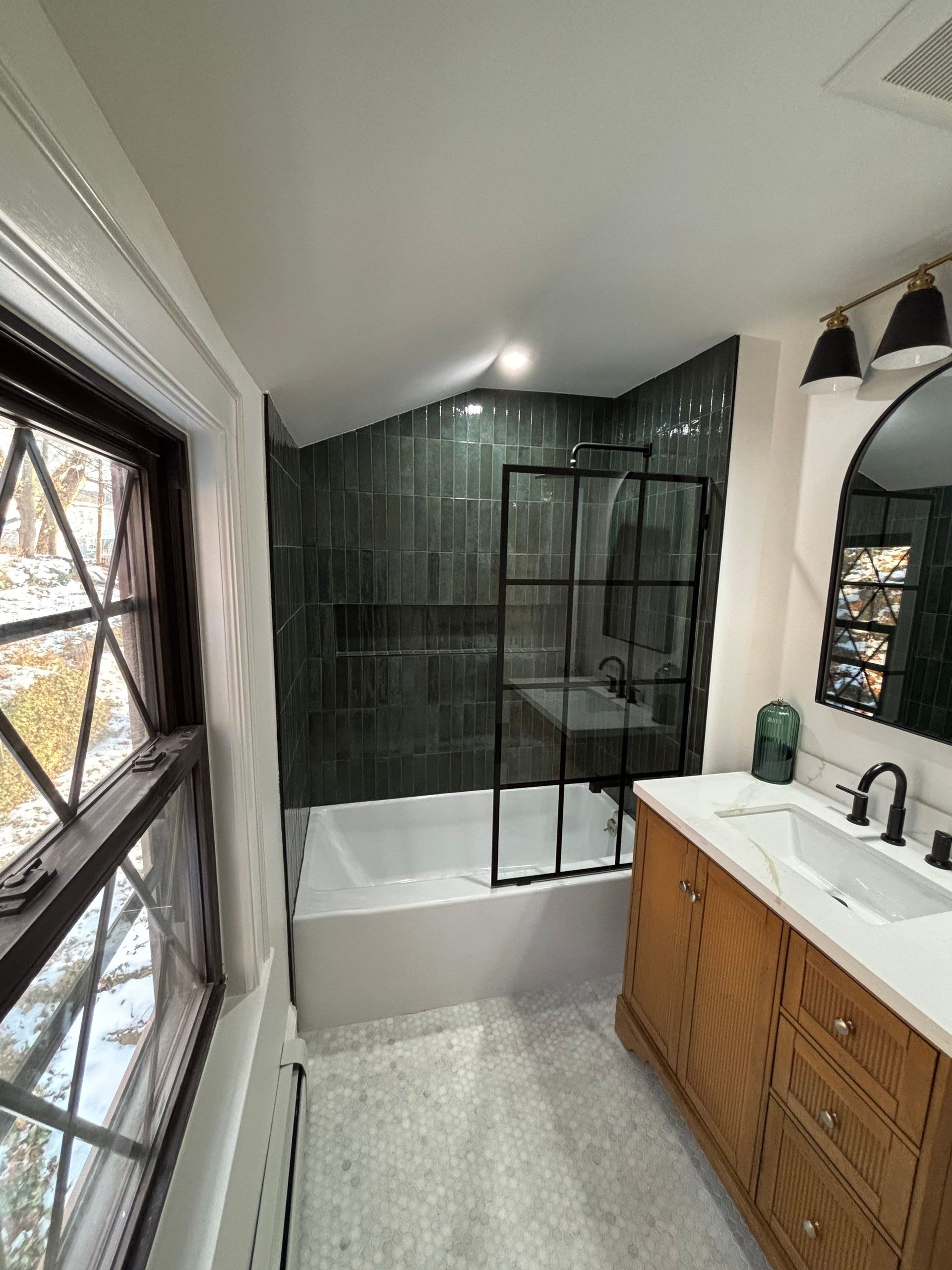 Bathroom with green tiled shower, wood vanity, and black framed shower door.