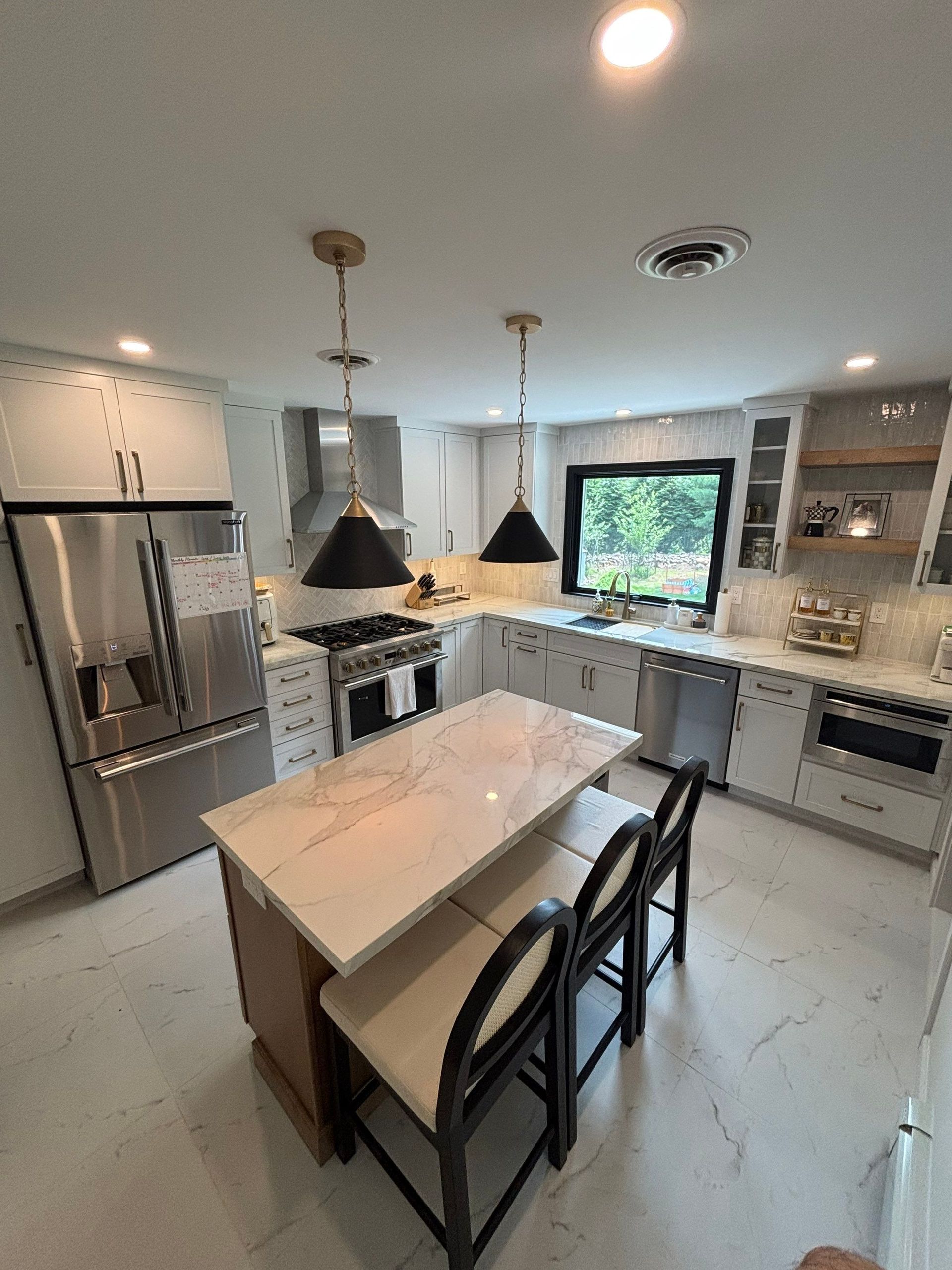 Modern kitchen with island, white cabinets, stainless steel appliances, and three black pendant lights.