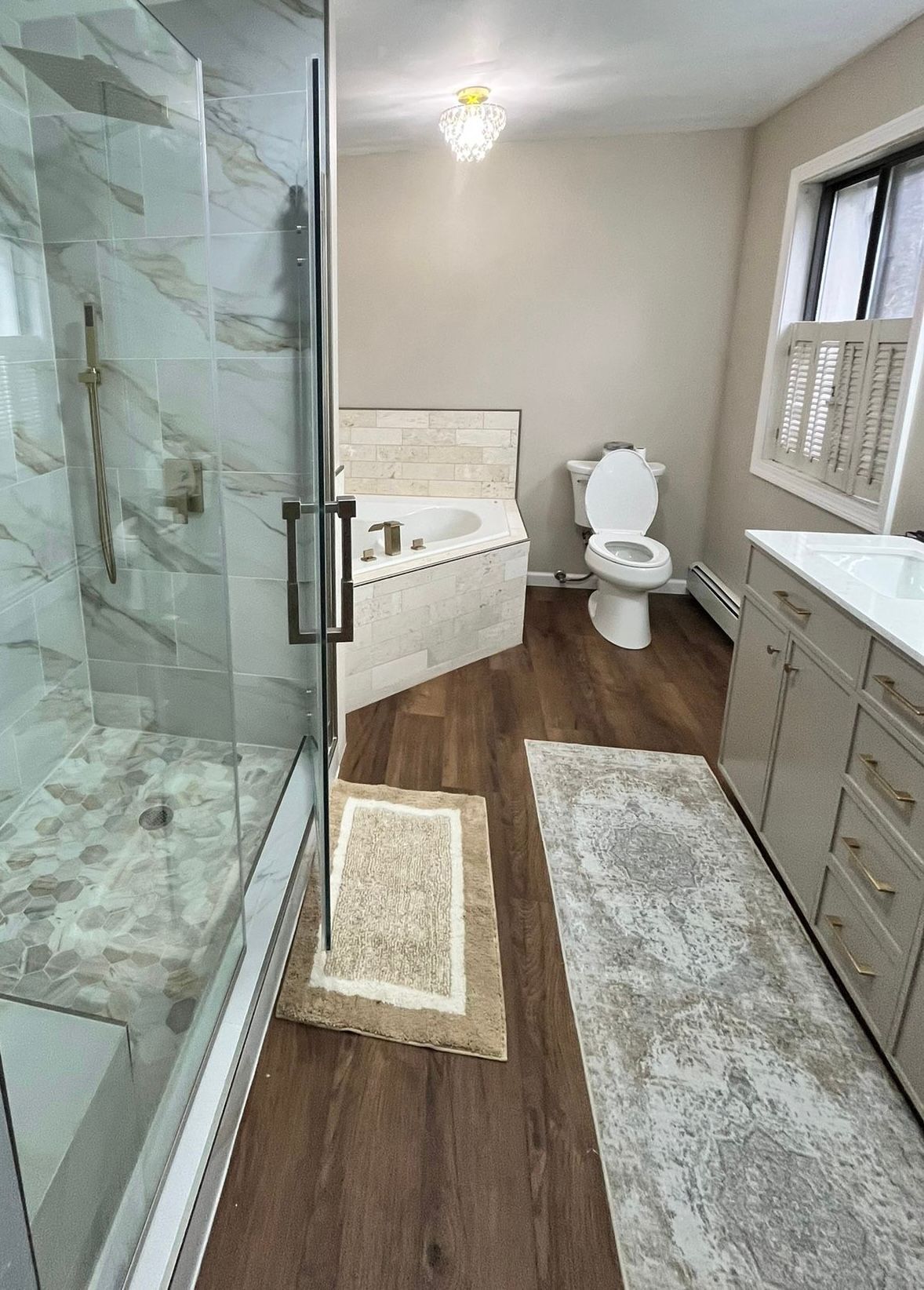 Bathroom with shower, tub, and vanity; tan walls, wood-look floor, and light-colored accents.
