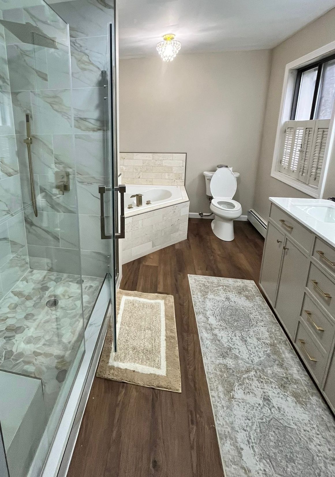 Modern bathroom with glass shower, tub, toilet, vanity, and beige walls, light wood floor.