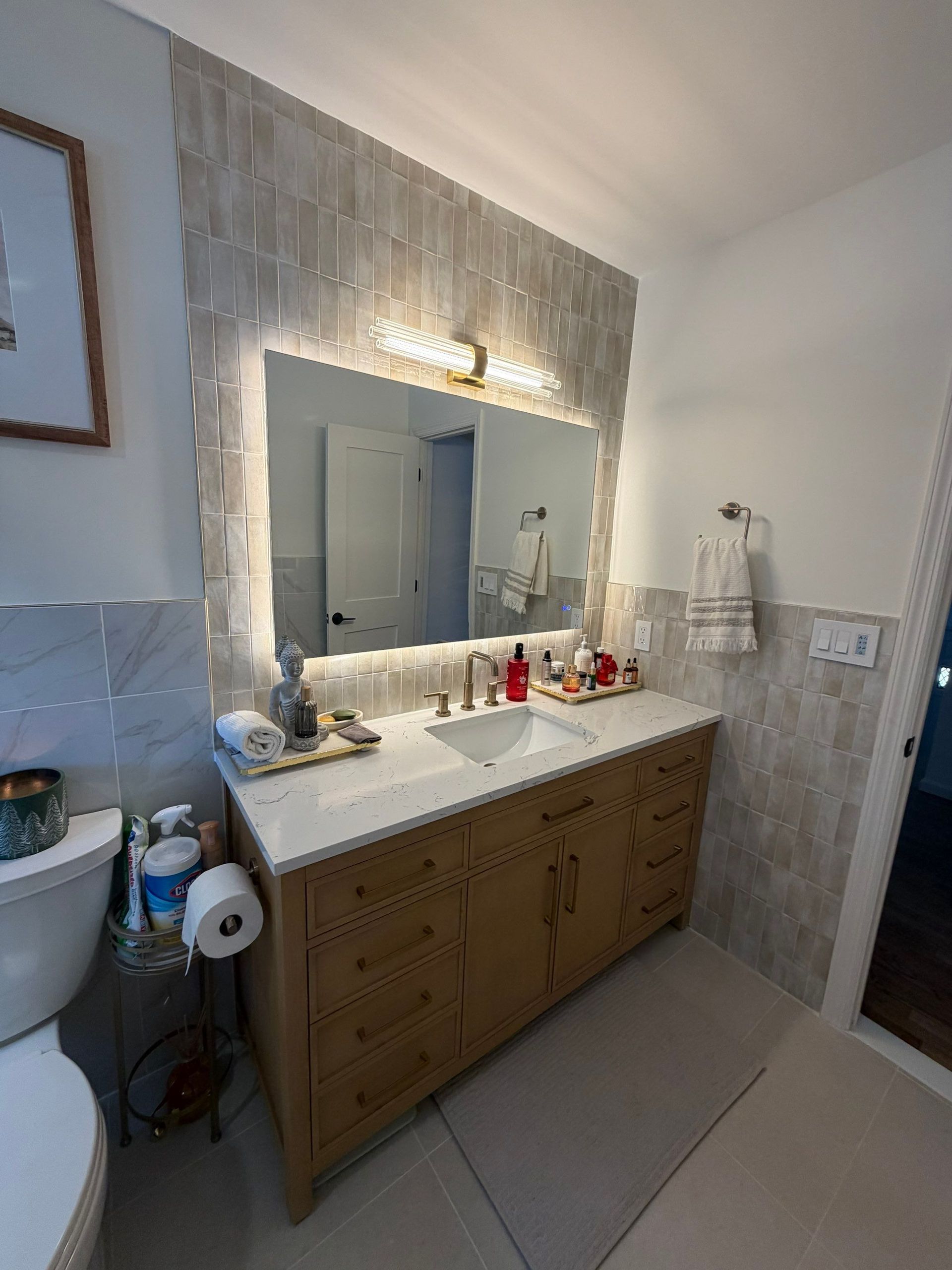 Bathroom with wooden vanity, large mirror, and tiled accent wall.