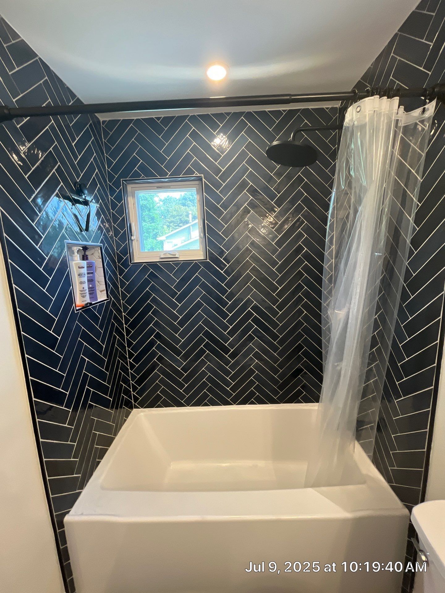 Bathroom with black herringbone tile, white tub, window, and shower curtain.