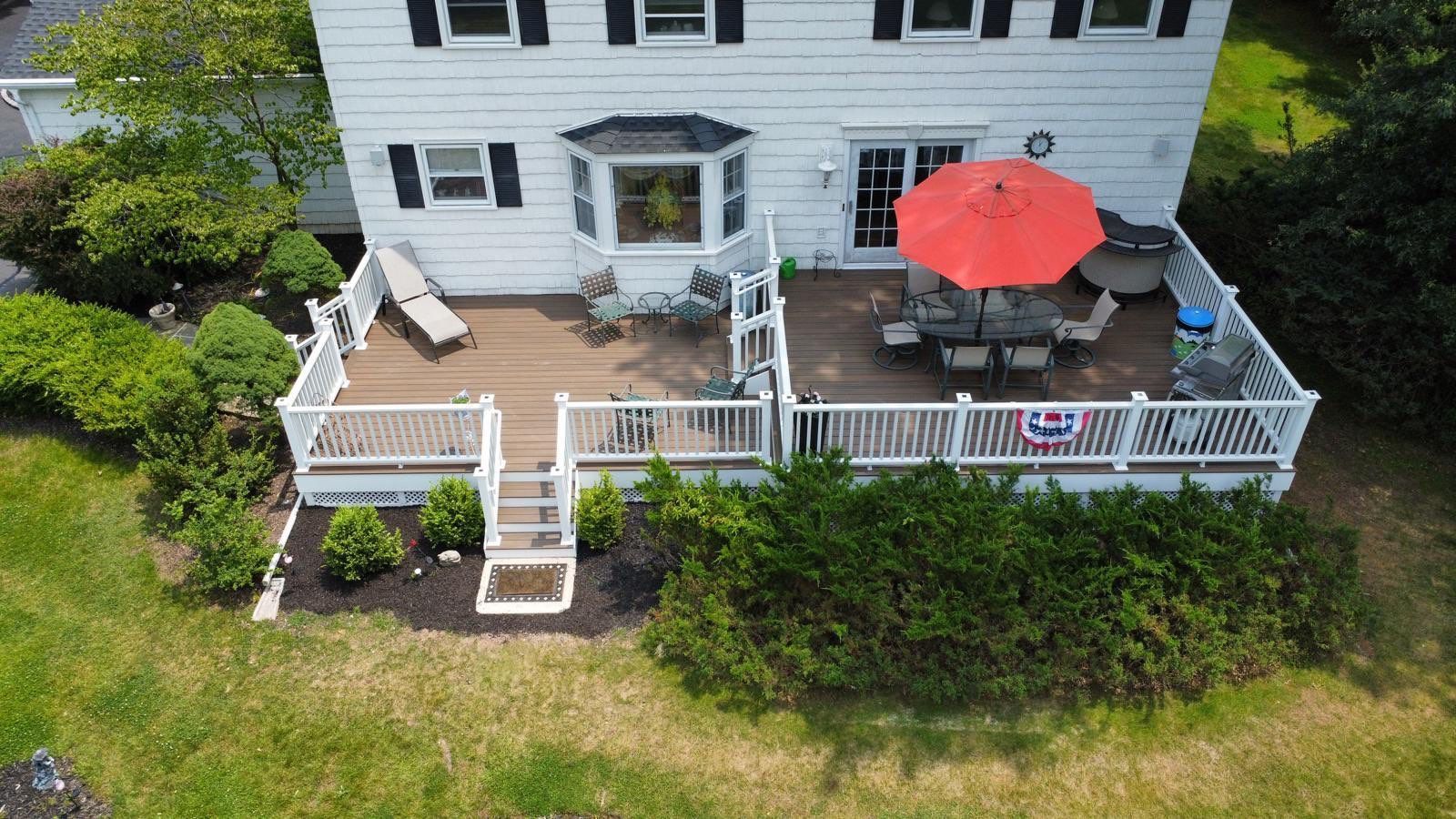 Elevated wooden deck attached to a white house. Orange umbrella shades outdoor dining set.