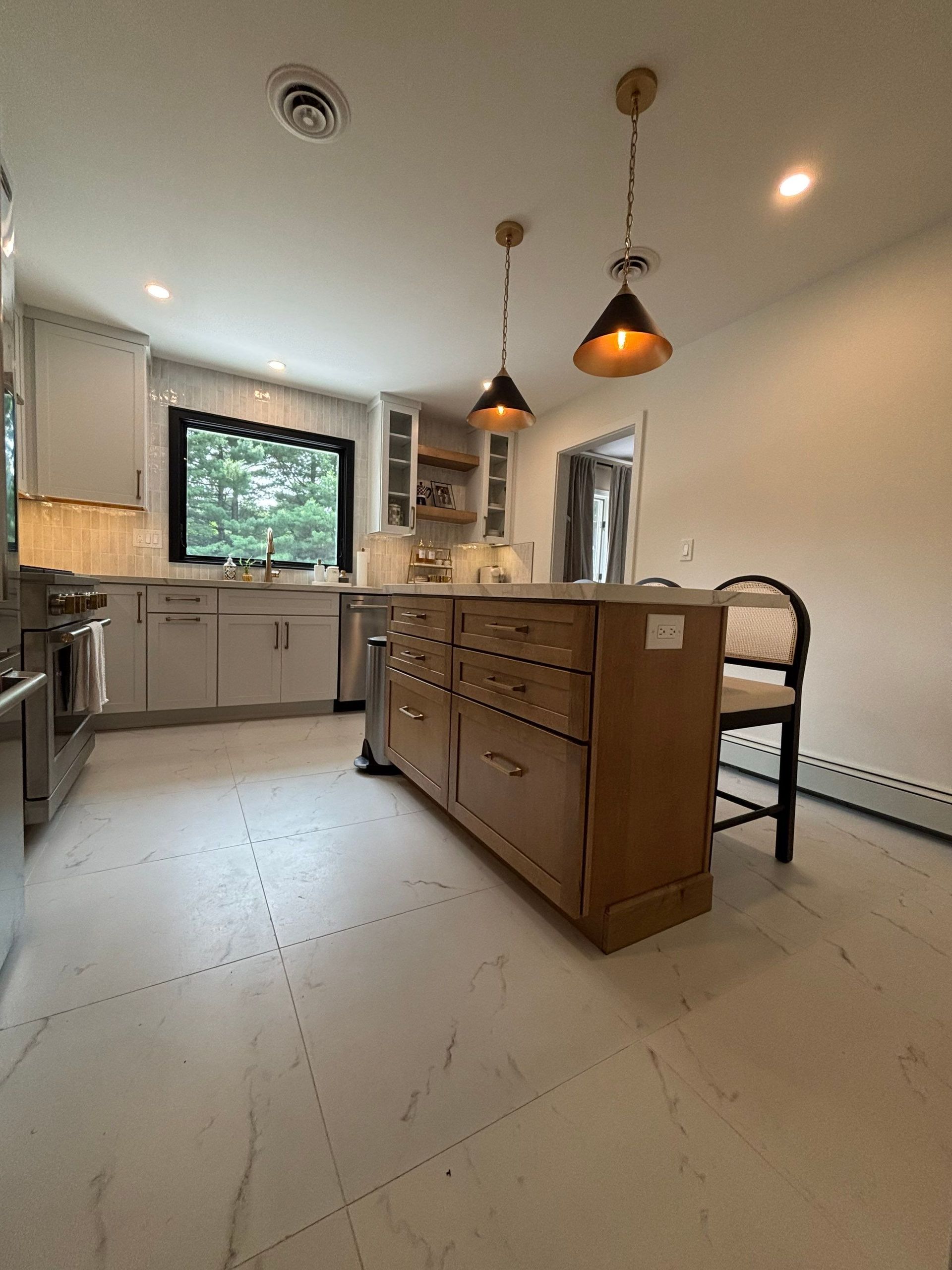 Kitchen with wooden island, pendant lights, white cabinets, large window, and a bar stool.