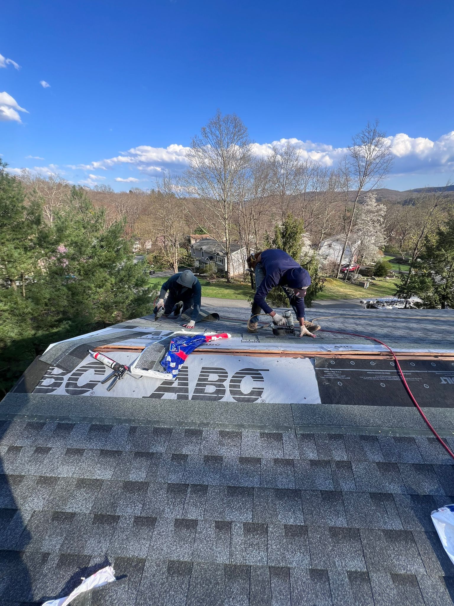 Three roofers installing shingles on a rooftop under a blue sky.