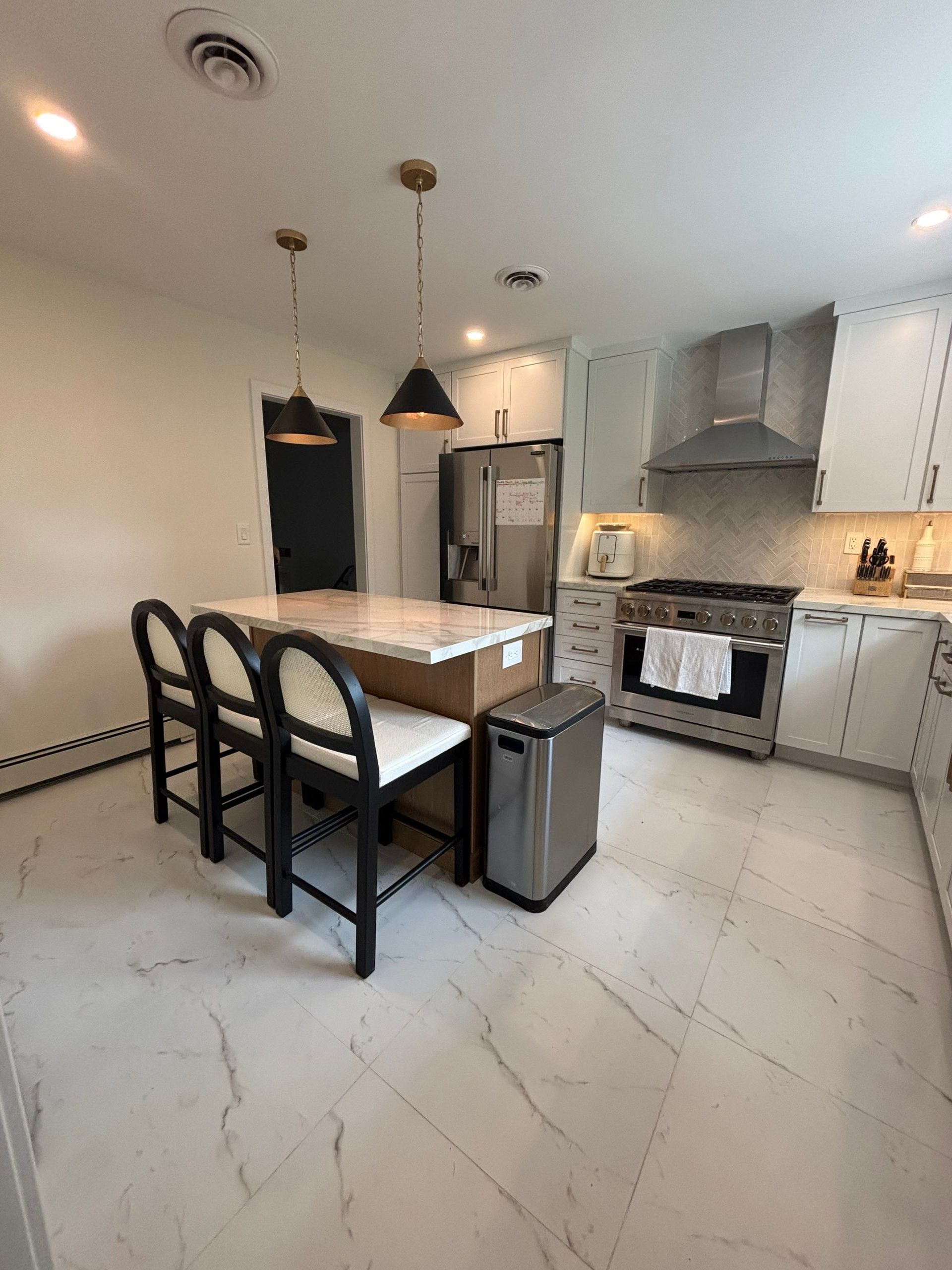 Modern kitchen with island seating, stainless steel appliances, and light marble flooring.