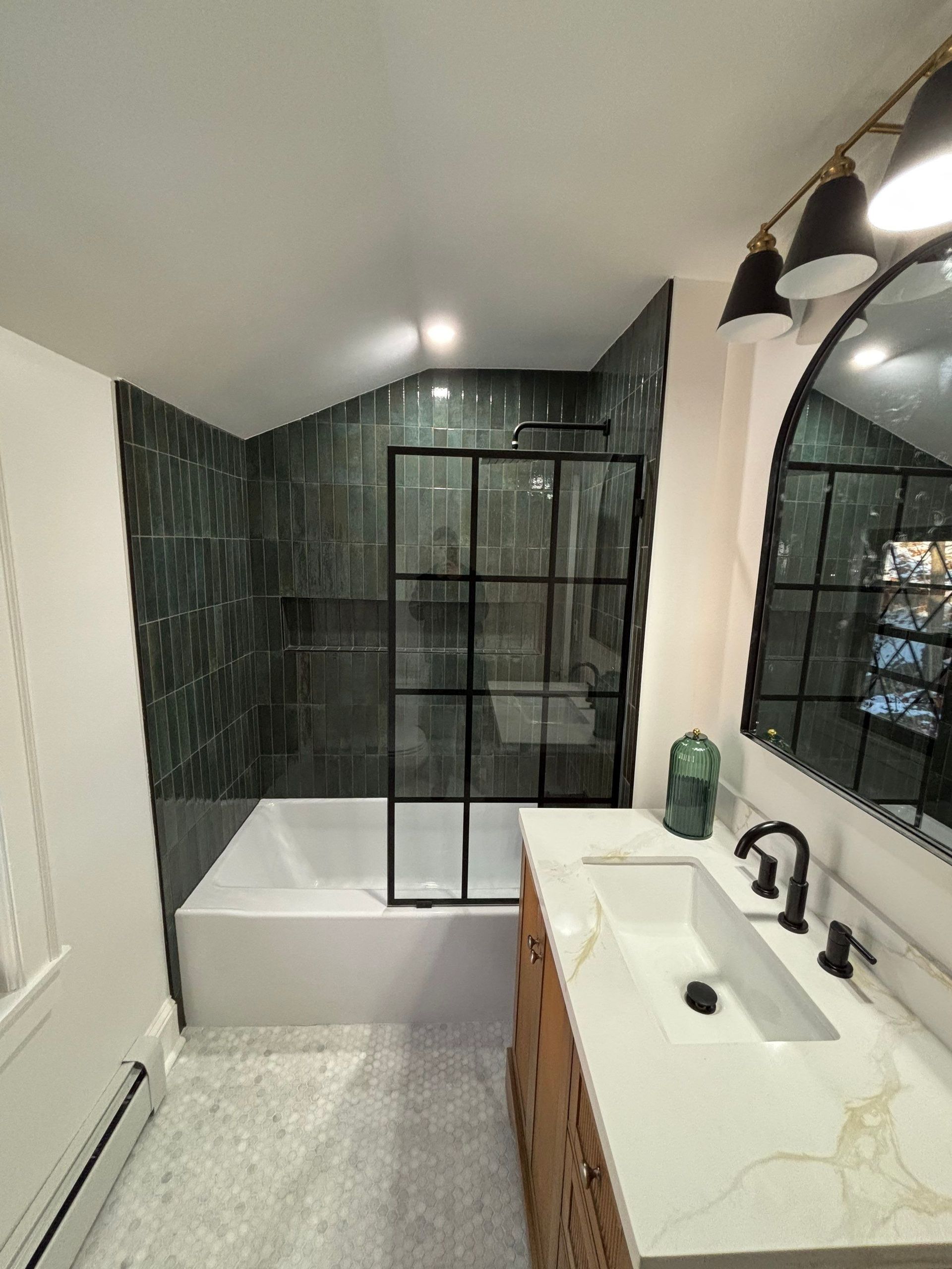 Bathroom remodel: Black-framed shower enclosure with green tile, white tub, vanity, and a large mirror.