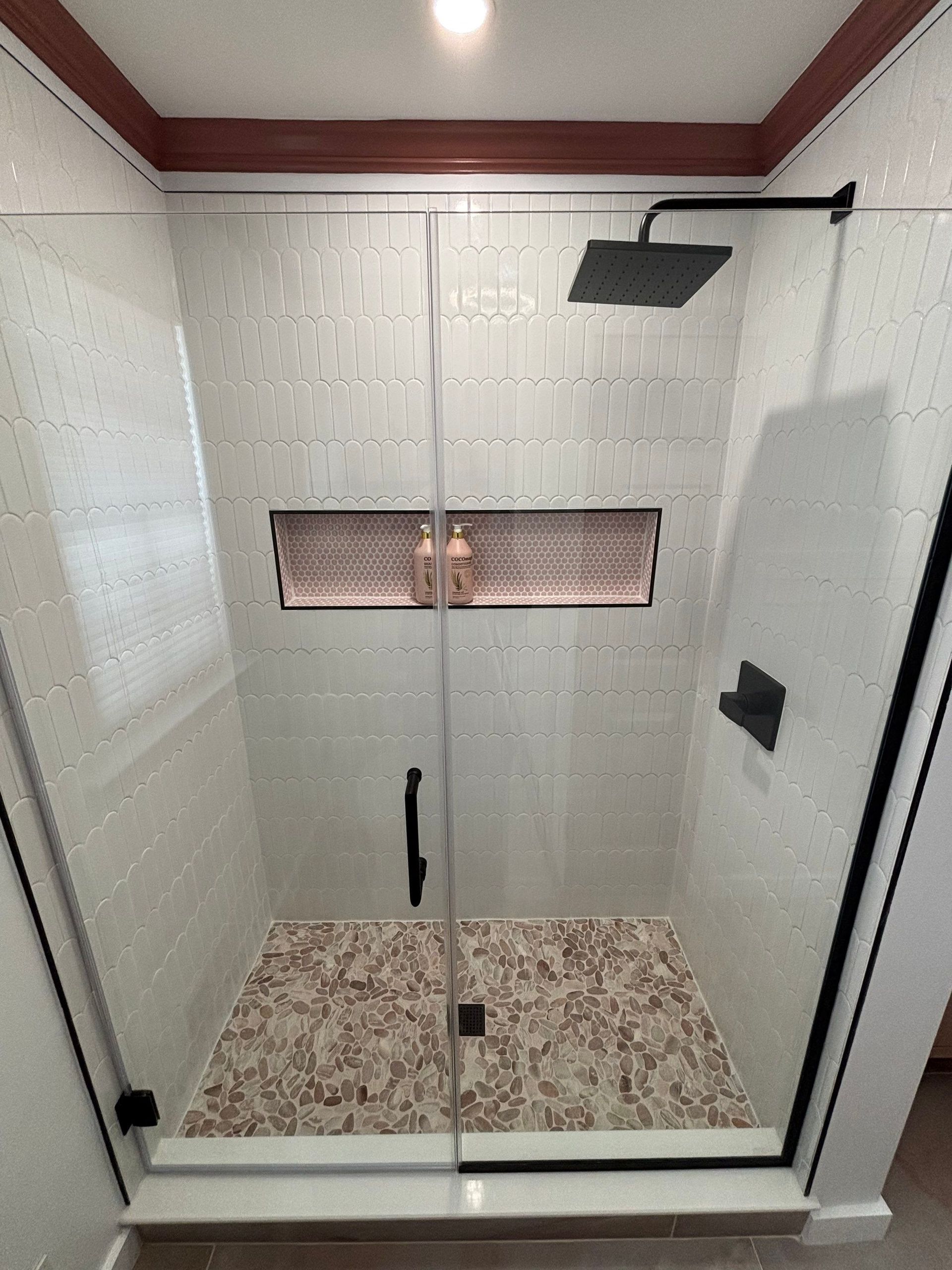 Modern shower with glass door, white tiles, brown accent niche, and floral floor pattern.