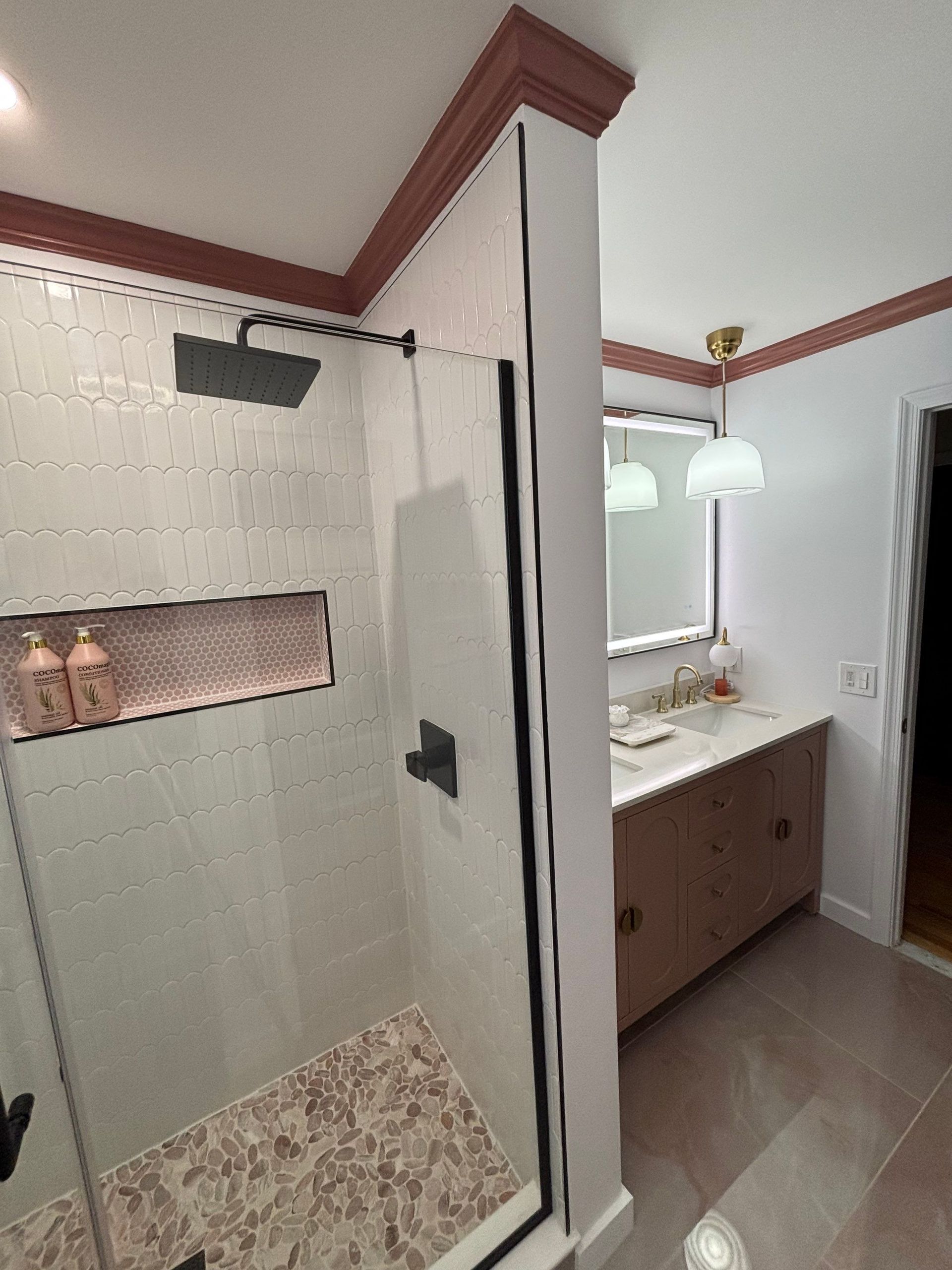 Bathroom with shower, vanity, and doorway. White walls, pink trim, and black shower fixtures.