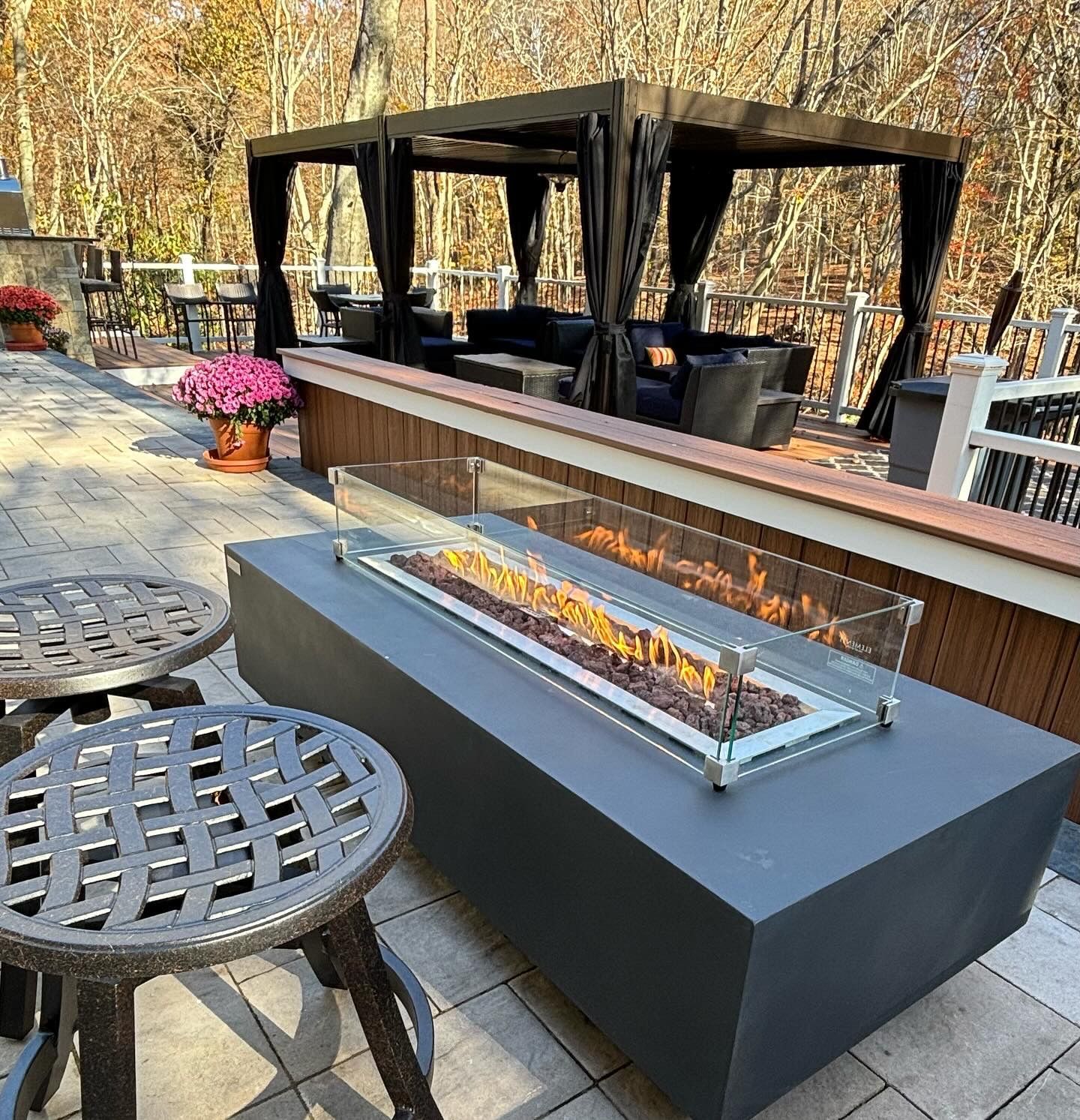 Patio with fire pit, lounge seating under a gazebo, and surrounding autumn foliage.