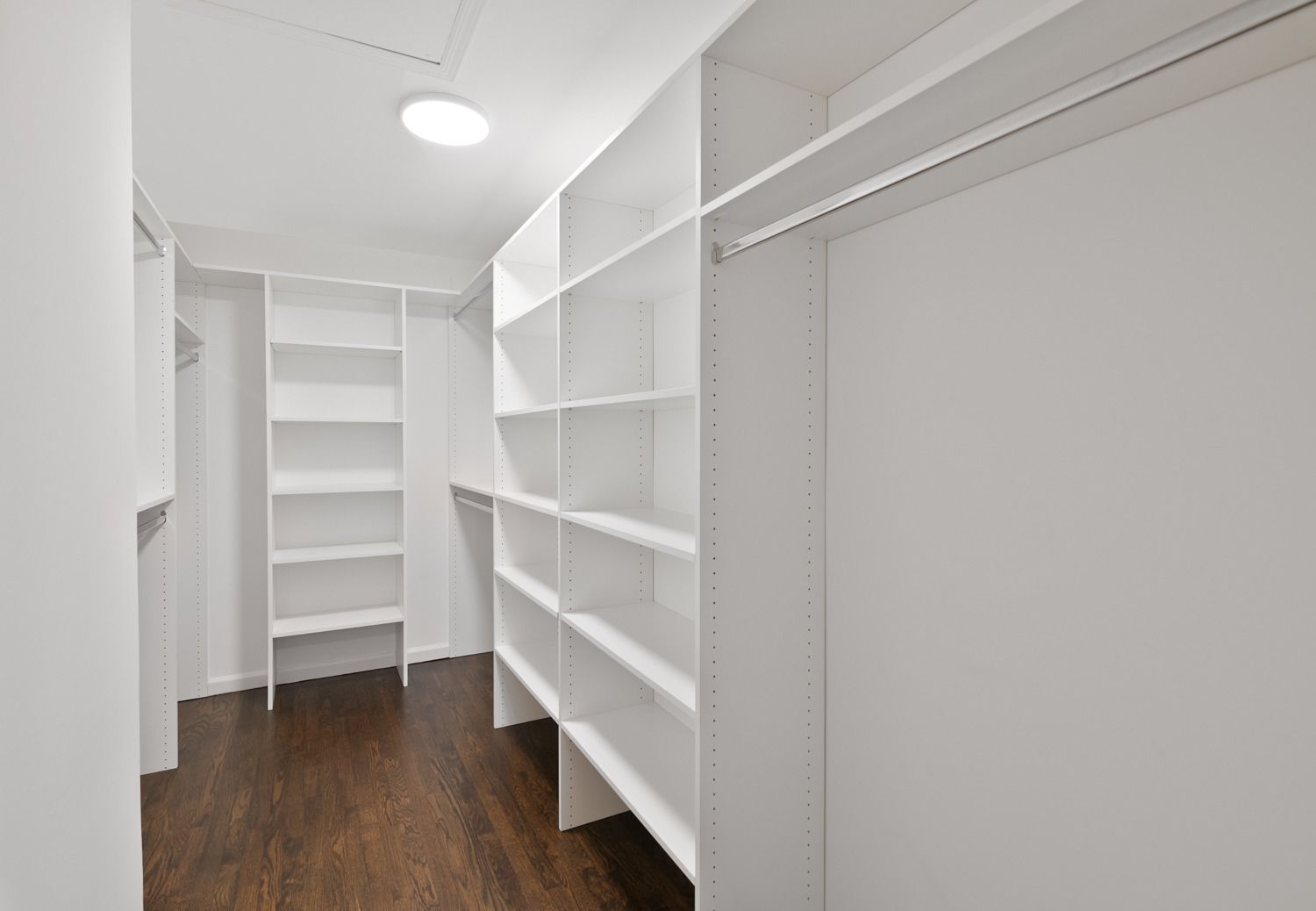Empty white closet with shelves and hanging rods; dark wood floor.