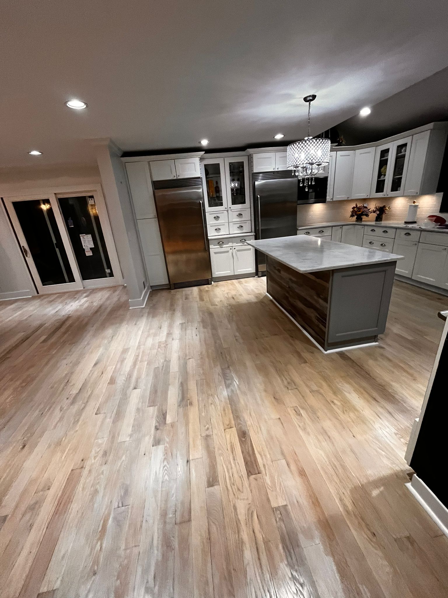 Spacious modern kitchen with wood floors, white cabinets, stainless steel appliances, and a gray island.