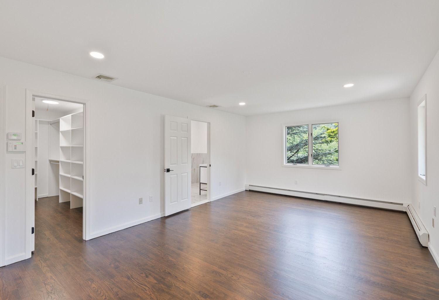 Empty bedroom with dark hardwood floors, white walls, and a walk-in closet.