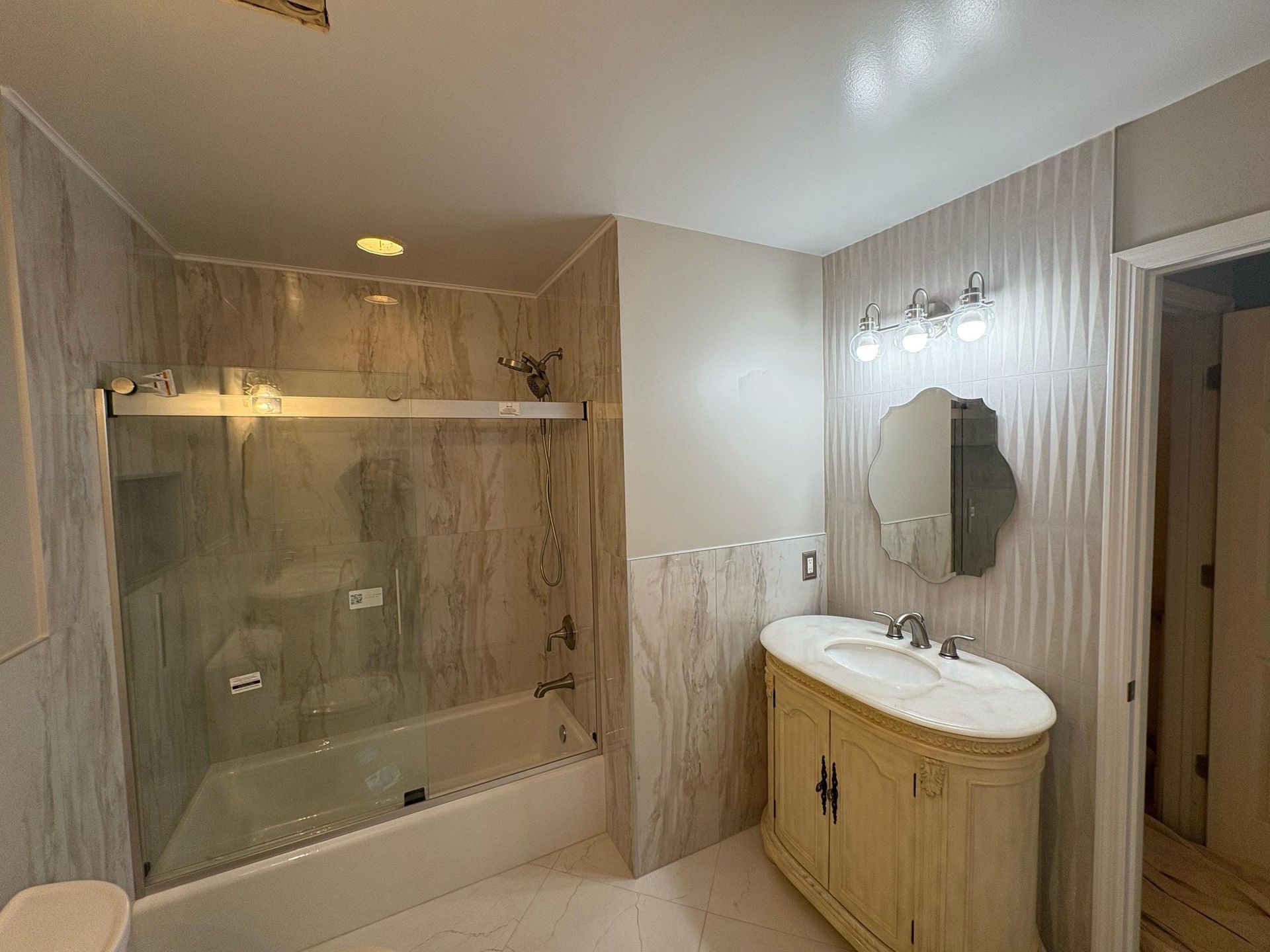 Bathroom with beige marble tile, a bathtub, sink, mirror, and a partially open door.