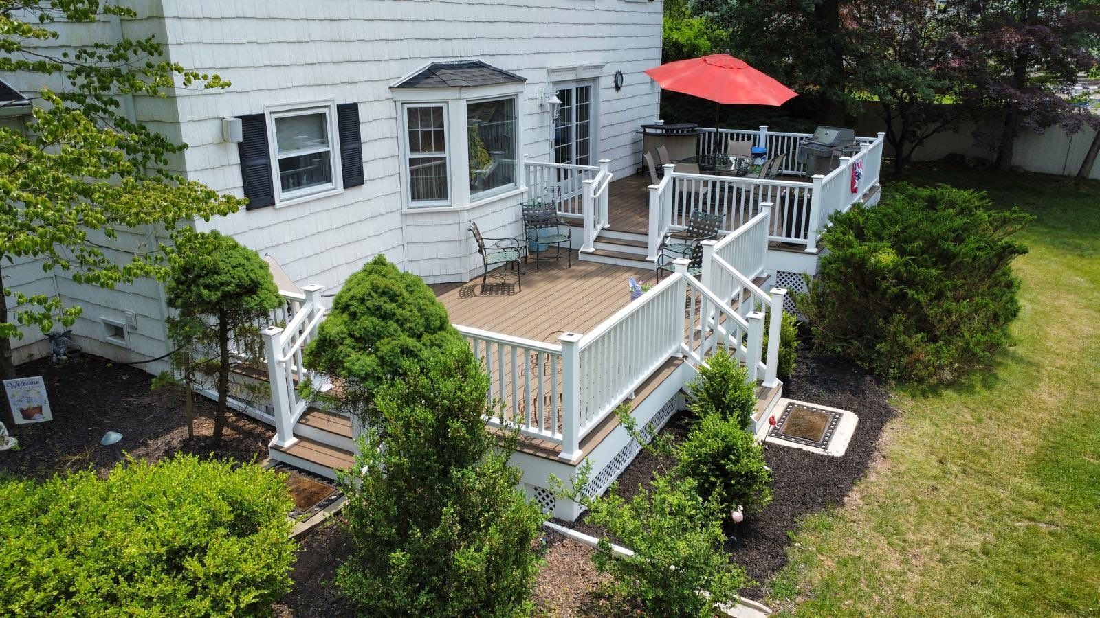 Backyard deck with white railings, bay window, and red umbrella.