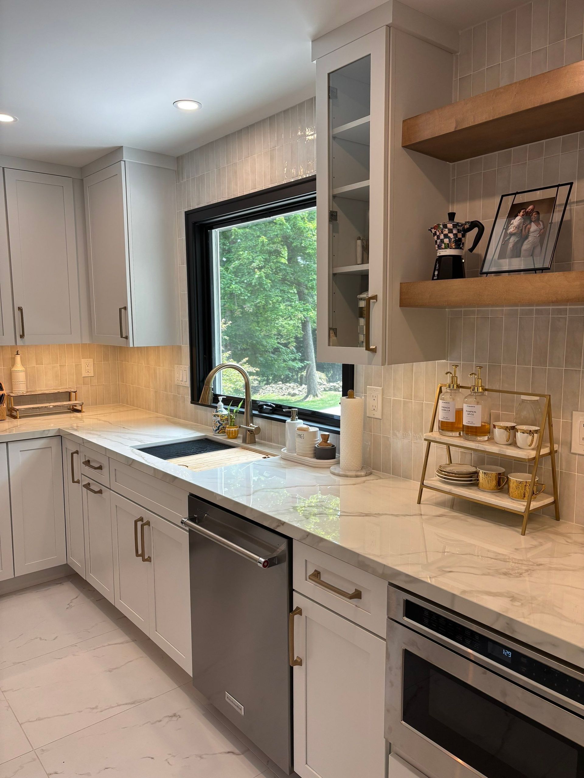 White kitchen with cabinets, stainless steel appliances, a window, and wooden shelves.