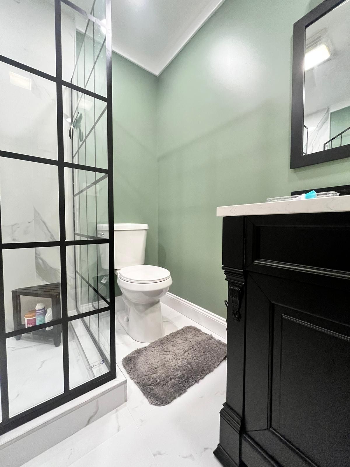 Modern bathroom with black accents, shower, toilet, green walls, and black vanity.