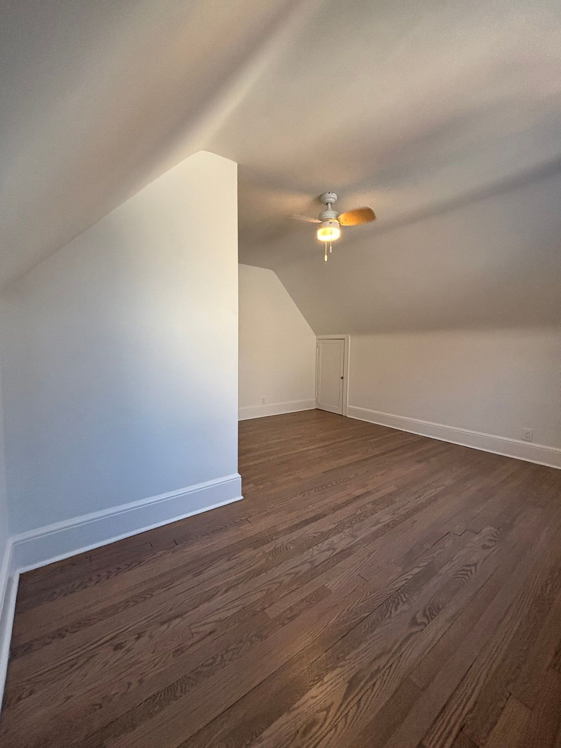 Attic room with hardwood floor, sloped walls, white trim, and a ceiling fan.