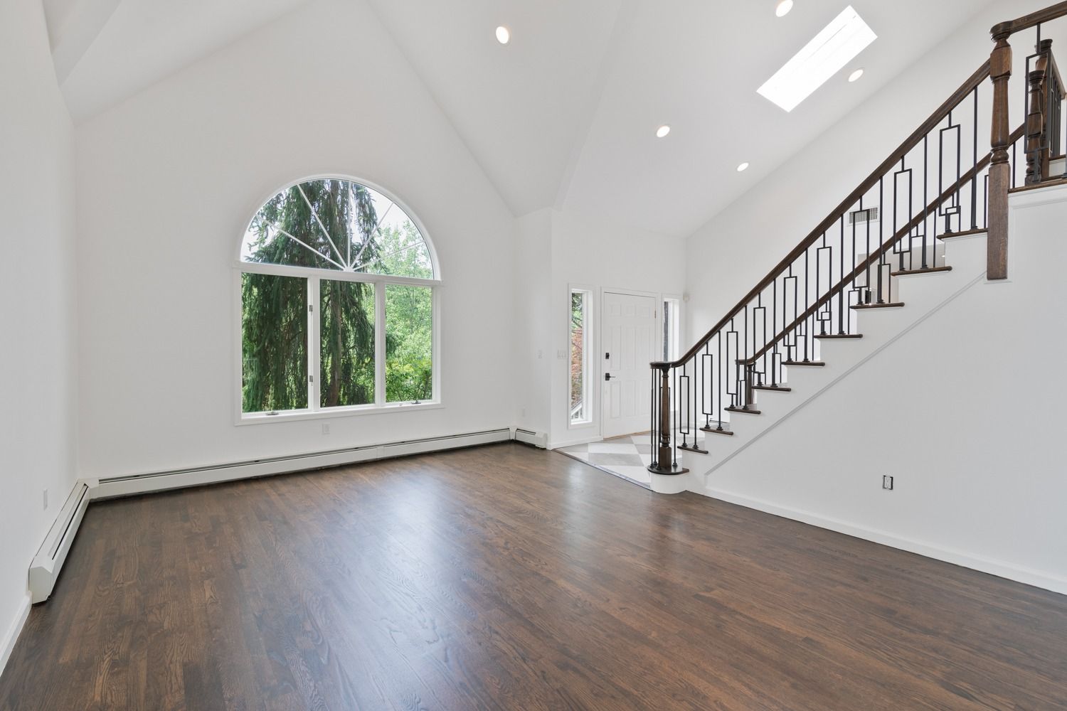 Spacious, empty entry hall with dark wood floors, a grand window, and a staircase.
