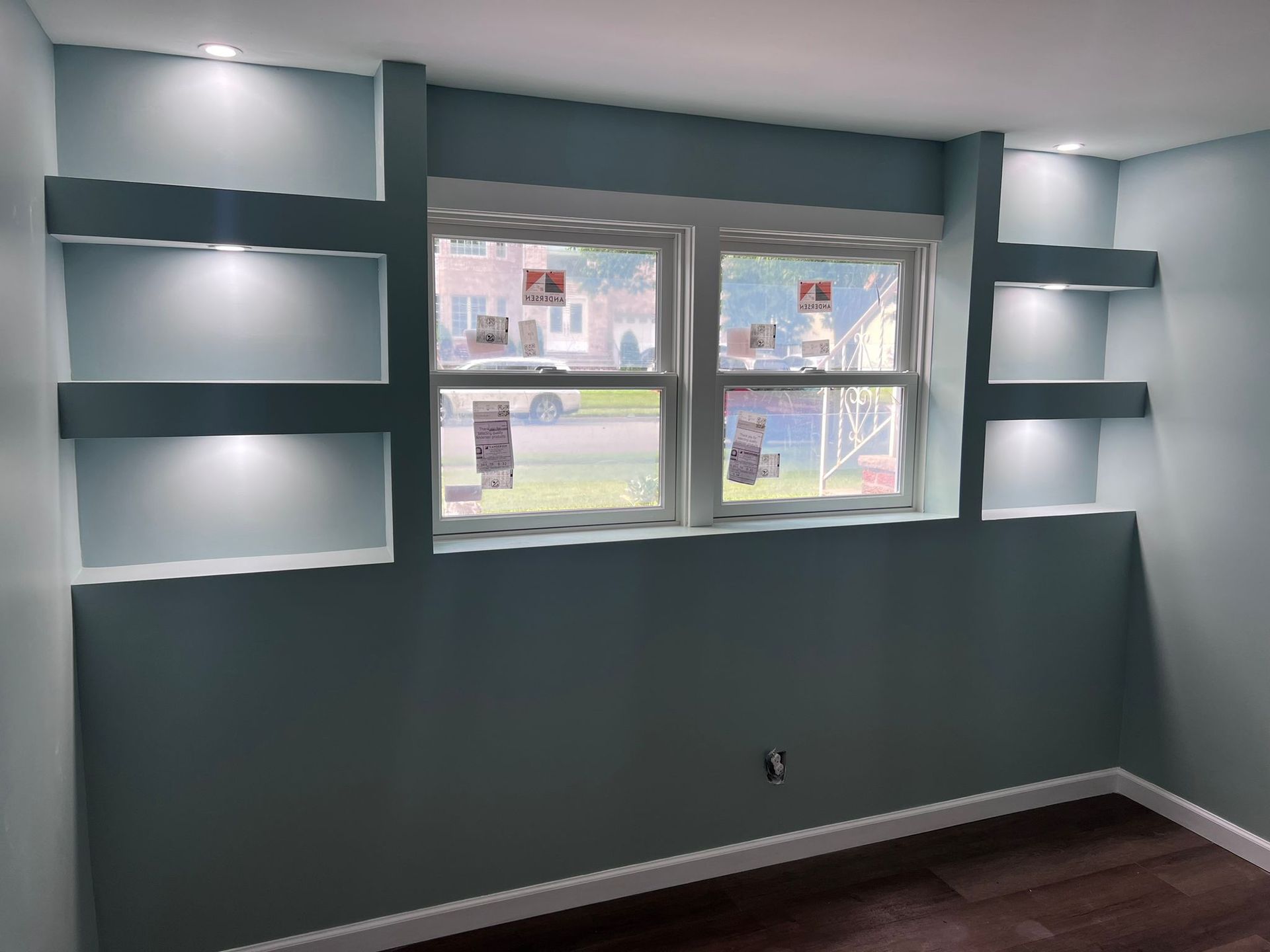 Blue wall with illuminated recessed shelves flanking a window; room with dark wood flooring.