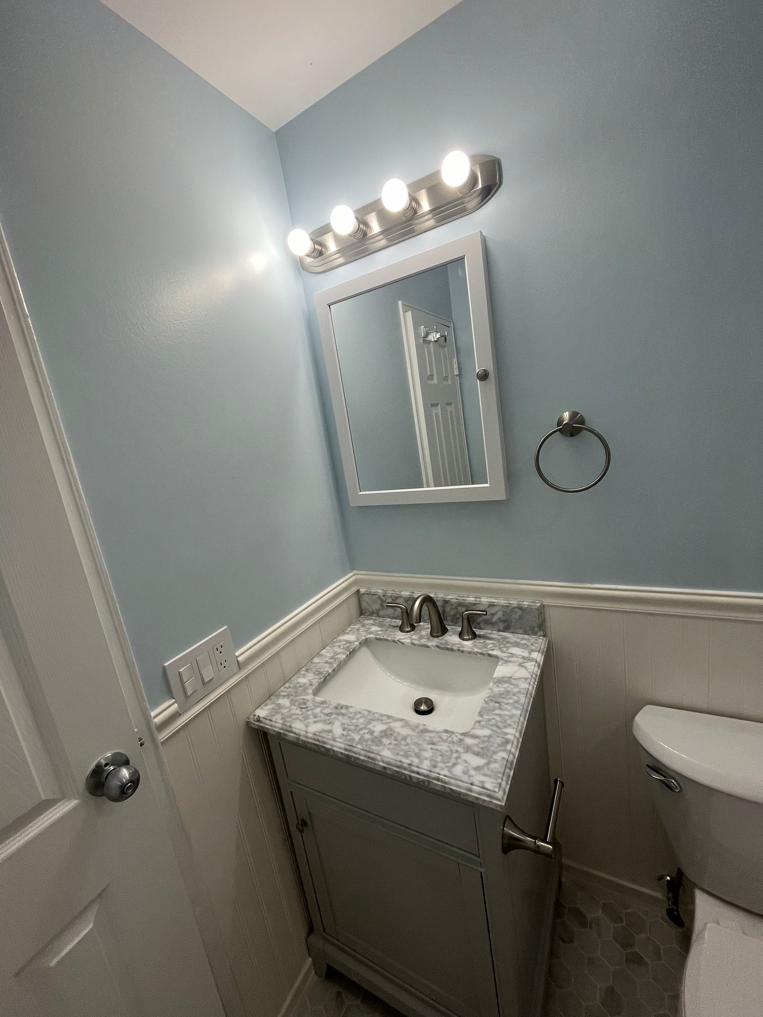 A small bathroom with a light blue wall, a vanity, and a toilet.