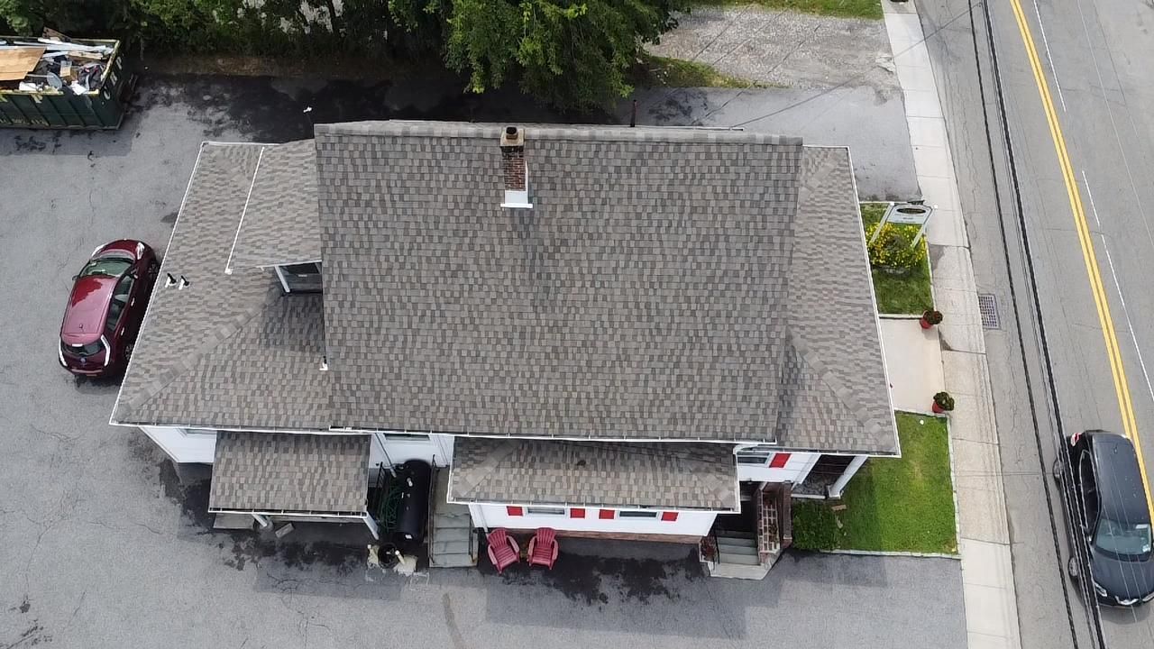 Overhead view of a building with a gray roof, a red car, a black car, and a road.