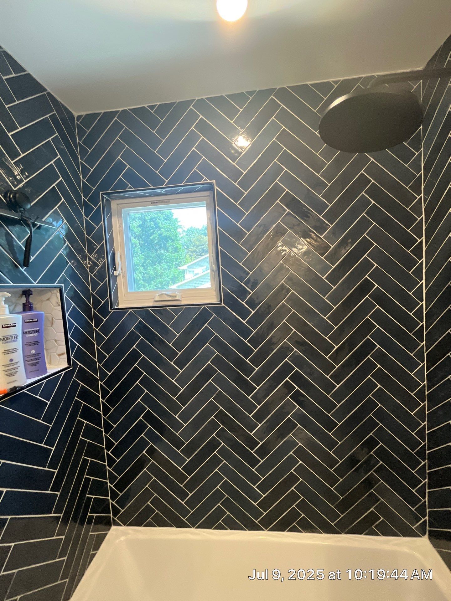 Dark blue herringbone tile shower with a small window, black shower head, and built-in shelf.