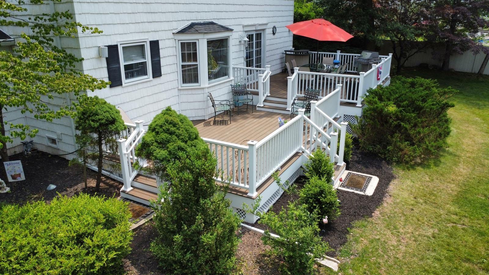 White house with a wooden deck and a red umbrella on a sunny day.